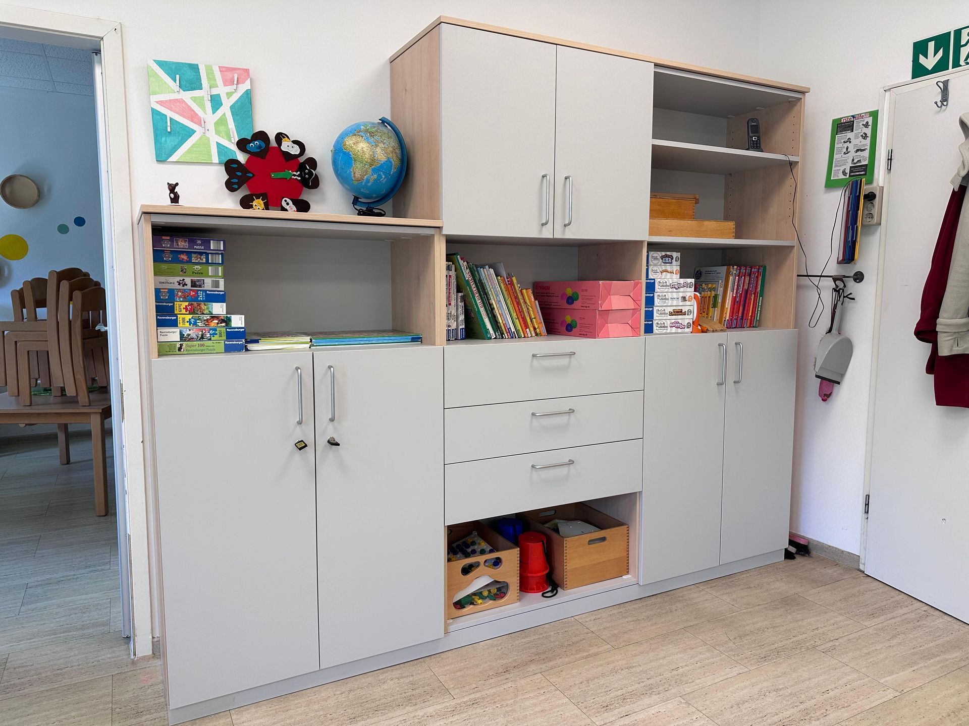 Aufbewahrungsschränke im Klassenzimmer mit Spielzeug, Büchern und einem Globus vor einer weißen Wand