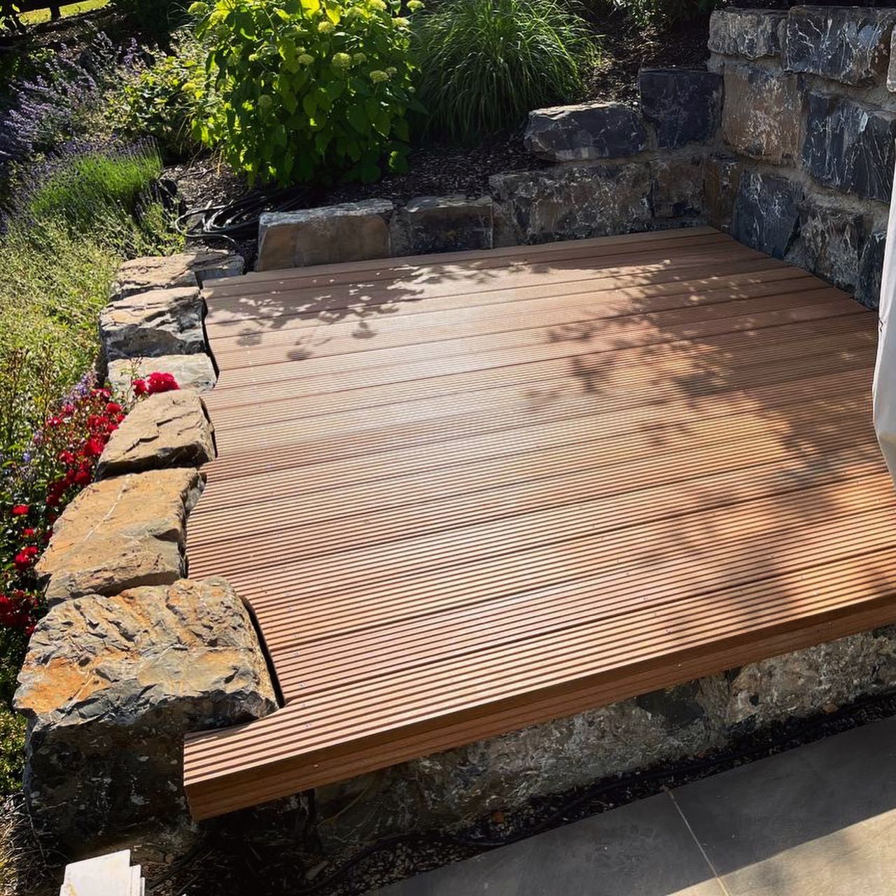 Holzterrasse mit Steineinfassung neben einem Garten und einer Steinmauer