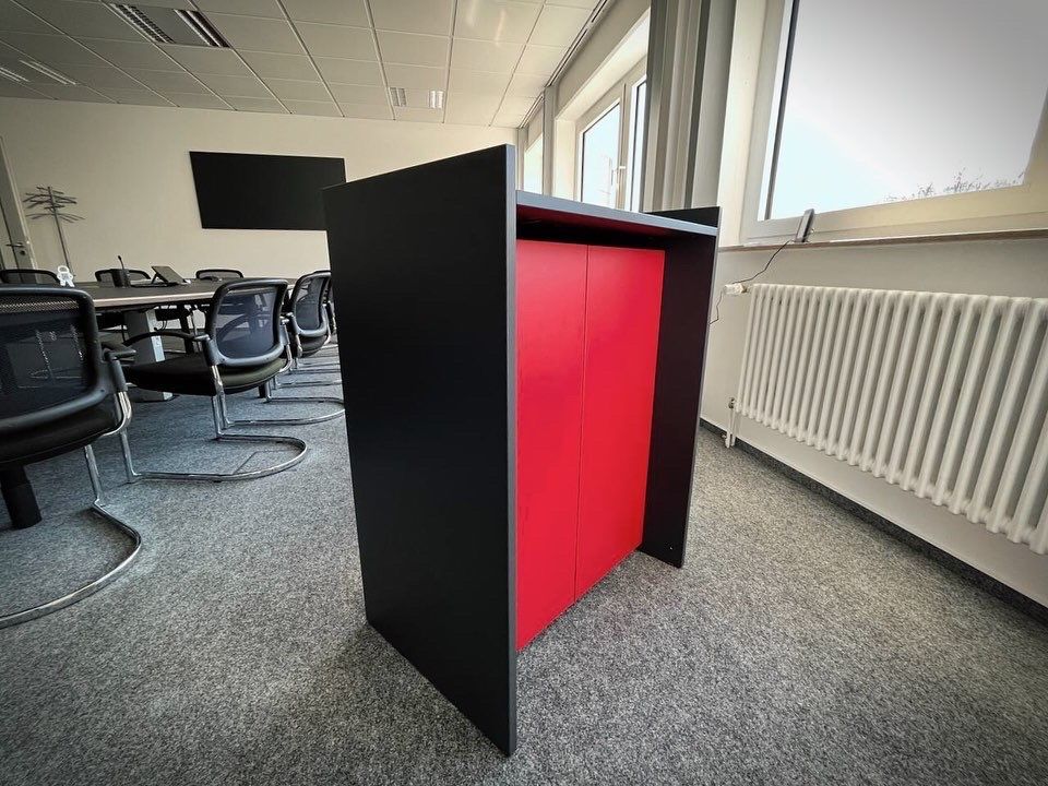 Schwarzes und rotes Rednerpult in einem Klassenzimmer mit Stühlen und Fenstern im Hintergrund