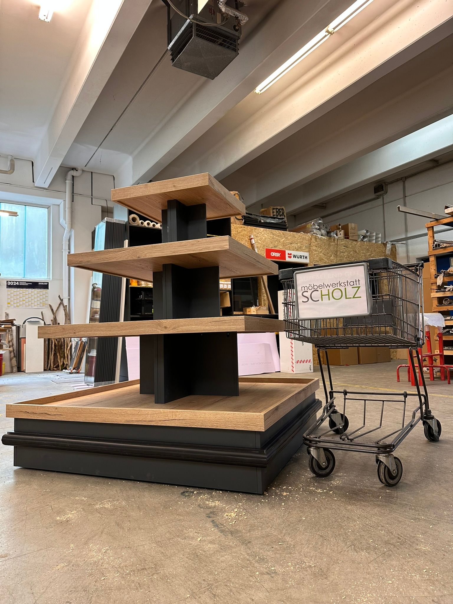 Mehrstöckige Ausstellungsstruktur aus Holz in einer hellen Werkstatt, in der Nähe Wagen und Werkzeuge.