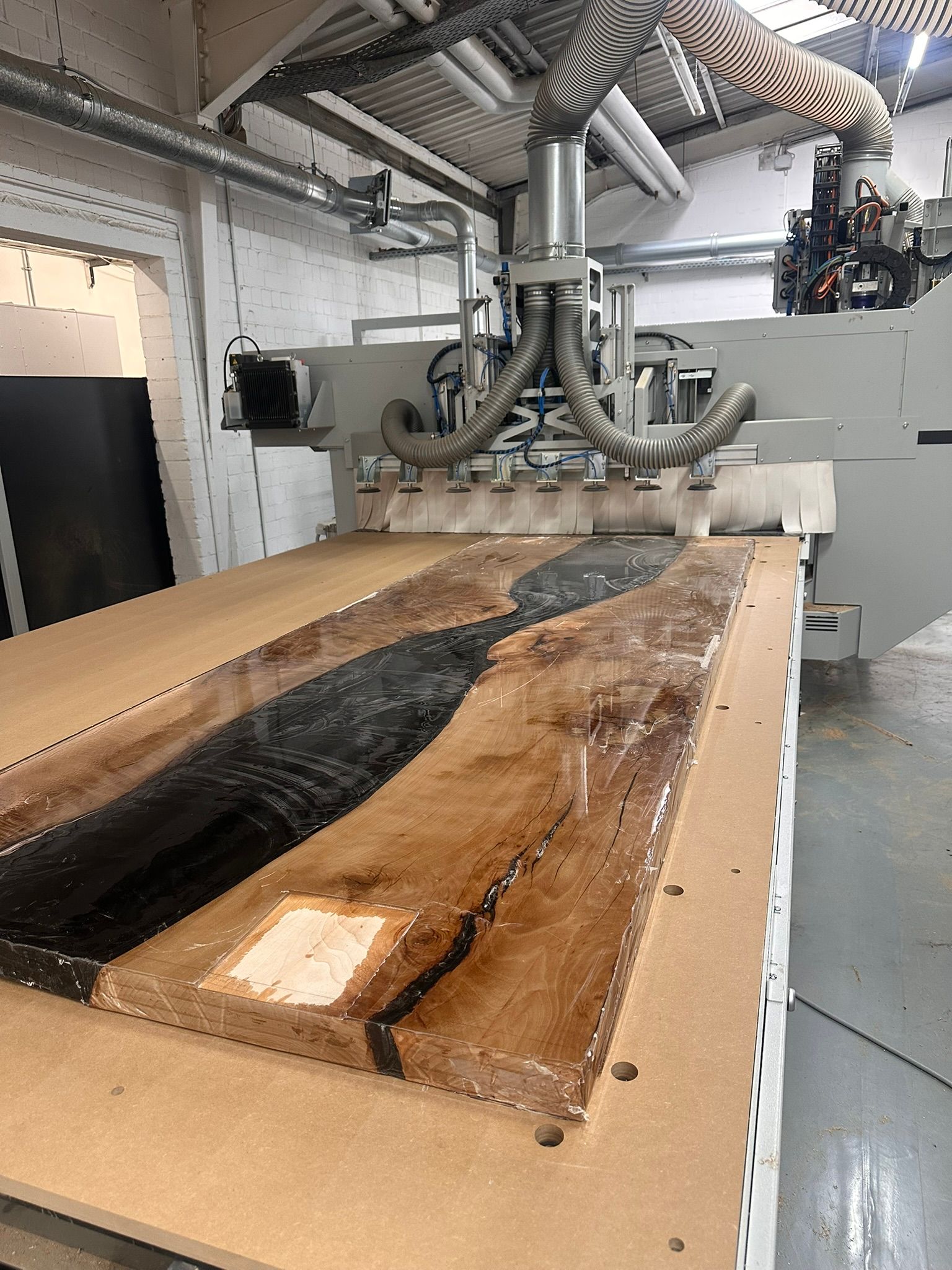 Eine industrielle CNC-Maschine bearbeitet in einer Werkstatt eine lange Holzplatte.