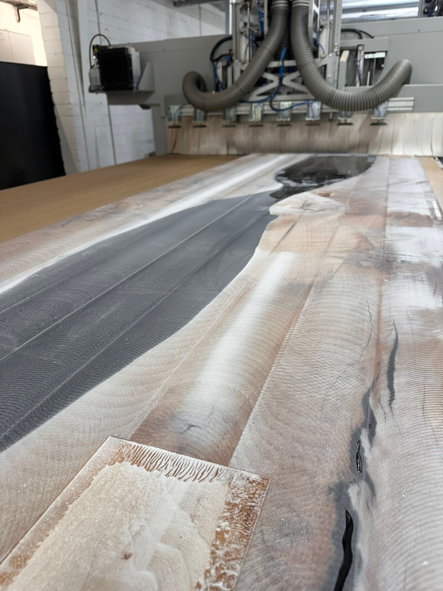 Staubiger Werkstattboden mit einem langen grauen Streifen und weißem Pulver in der Nähe der darüberliegenden Industrieschläuche.