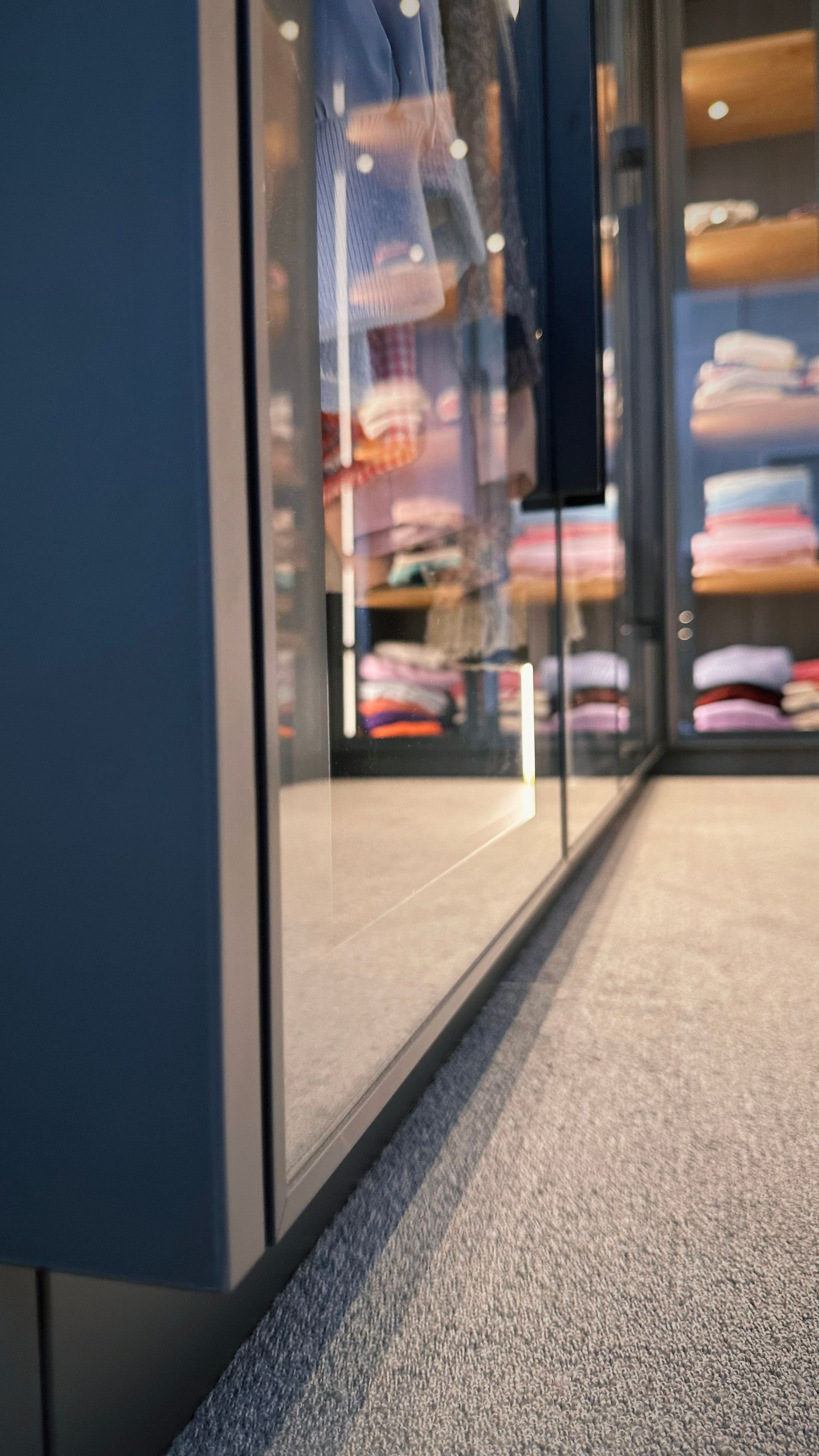 Ein Kleiderschrank mit Glastüren und Regalen voller ordentlich gefalteter Kleidung und Schuhe in einem sanft beleuchteten Raum