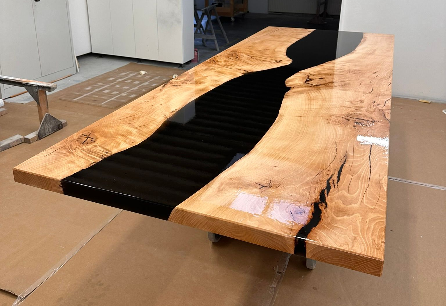 Mit Harz gefüllte Holztischplatte mit schwarzem Flussmuster, die in einer Werkstatt auf Karton ruht