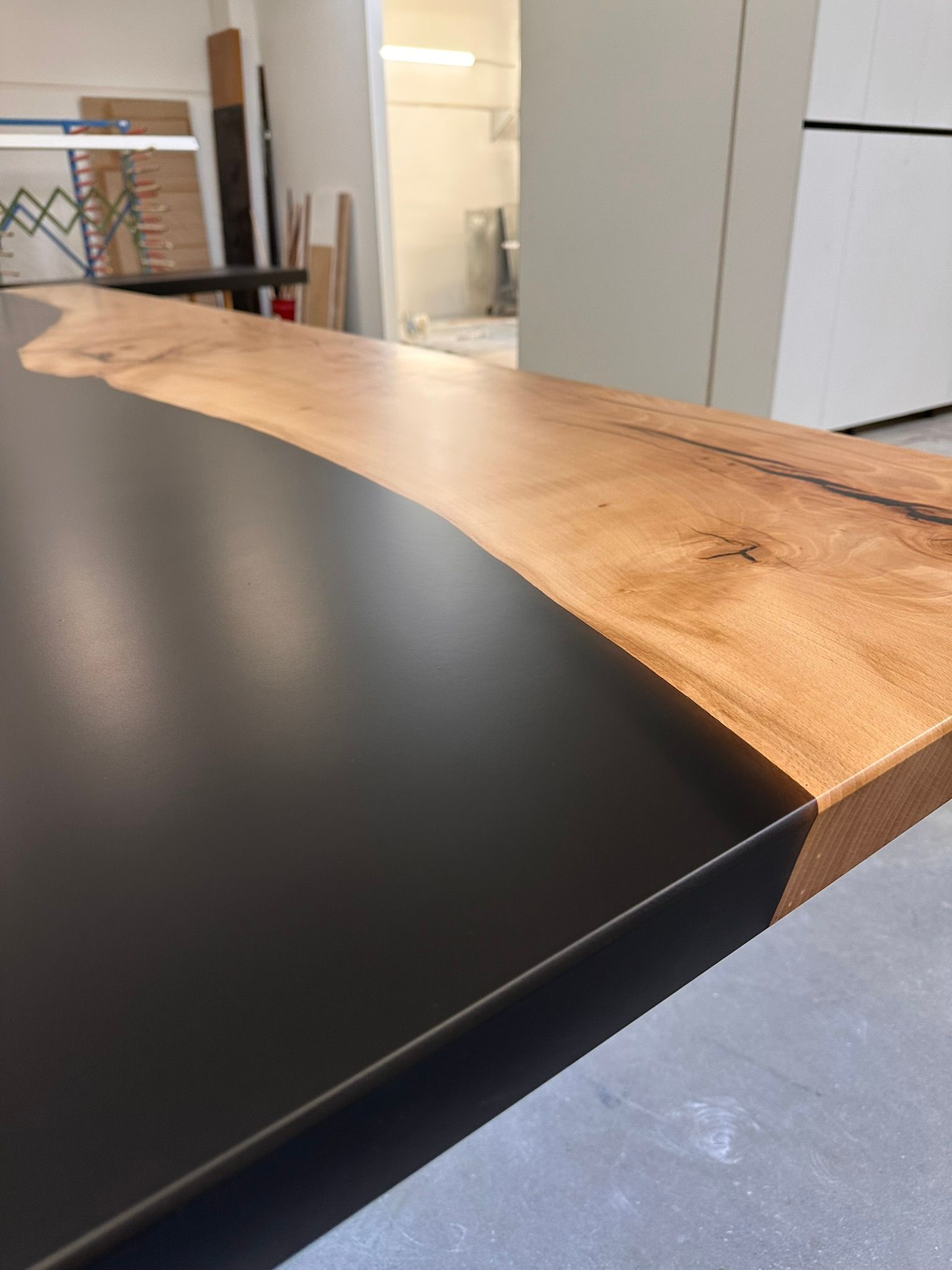Holztischplatte mit dunklem Epoxidharz-Bereich, gezeigt in einer Werkstatt- oder Ausstellungsraumumgebung