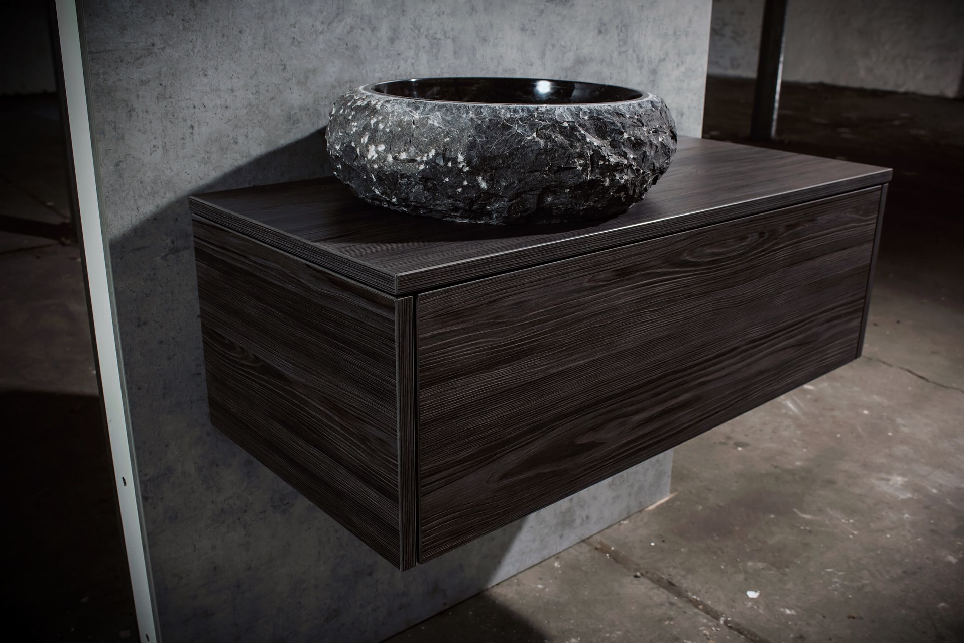 Dunkler, wandmontierter Waschtisch aus Holz mit schwarzem Steinwaschbecken in einem Badezimmer aus Beton