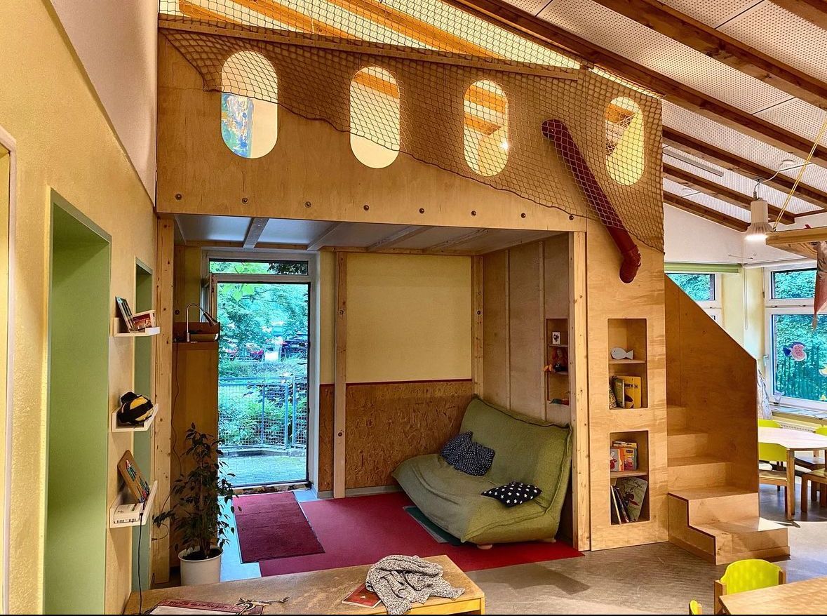 Gemütliches Loft-Wohnzimmer mit grünem Sofa, Holztreppe und offener Tür zum Garten.