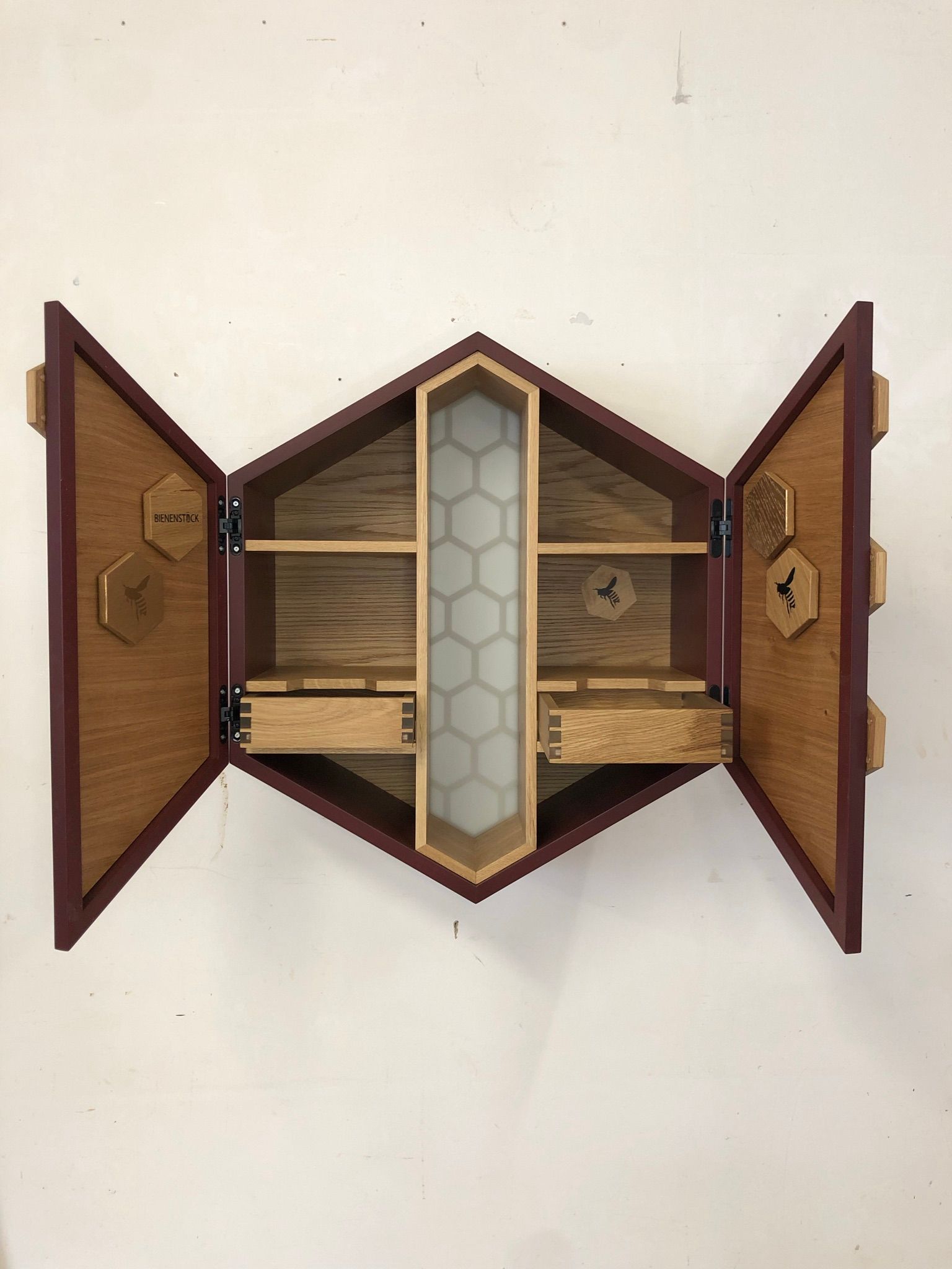 Offener hölzerner Wandschrank mit Spiegeltüren und Regalböden, an einer weißen Wand montiert.