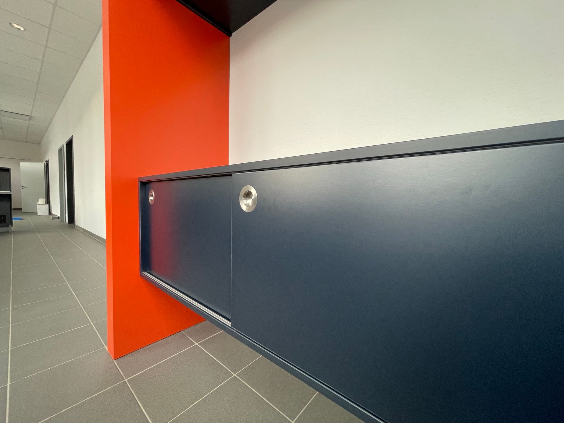 Flur mit orangefarbener Wand und einem langen, dunkelblauen Schrank oder einer Heizkörperverkleidung an der rechten Seite