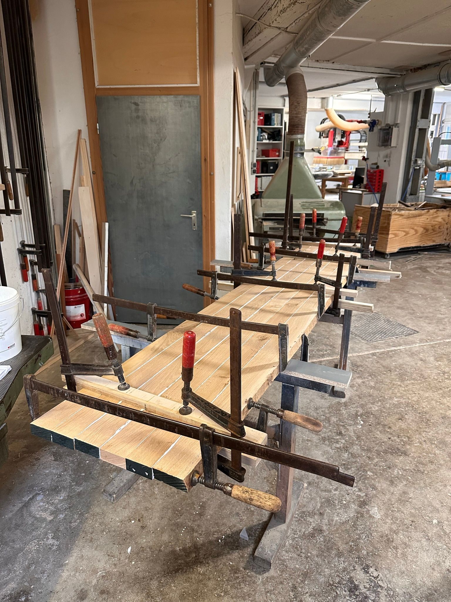 Holzwerkstatt mit mehreren auf Sägeböcken auf einem Betonboden befestigten Holzbrettern.