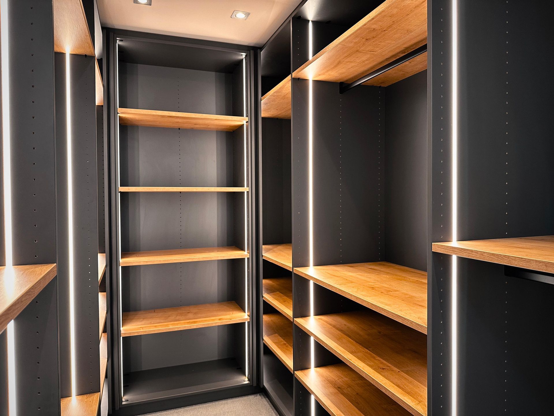 Leerer begehbarer Kleiderschrank mit dunklen Einbauregalen und warmen Holzregalen sowie Deckenbeleuchtung