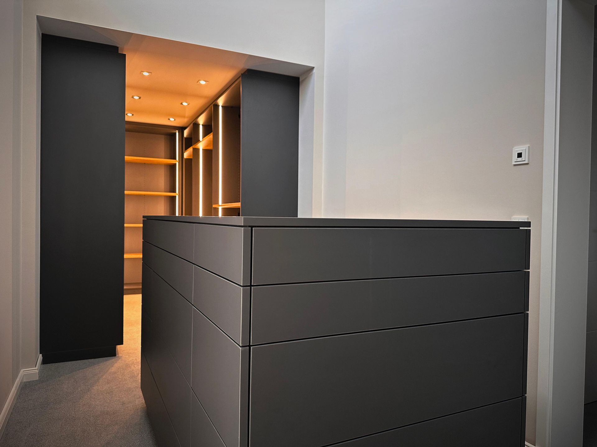 Moderner grauer Flur mit einem großen dunklen Schrank und warm beleuchteten Einbauregalen davor