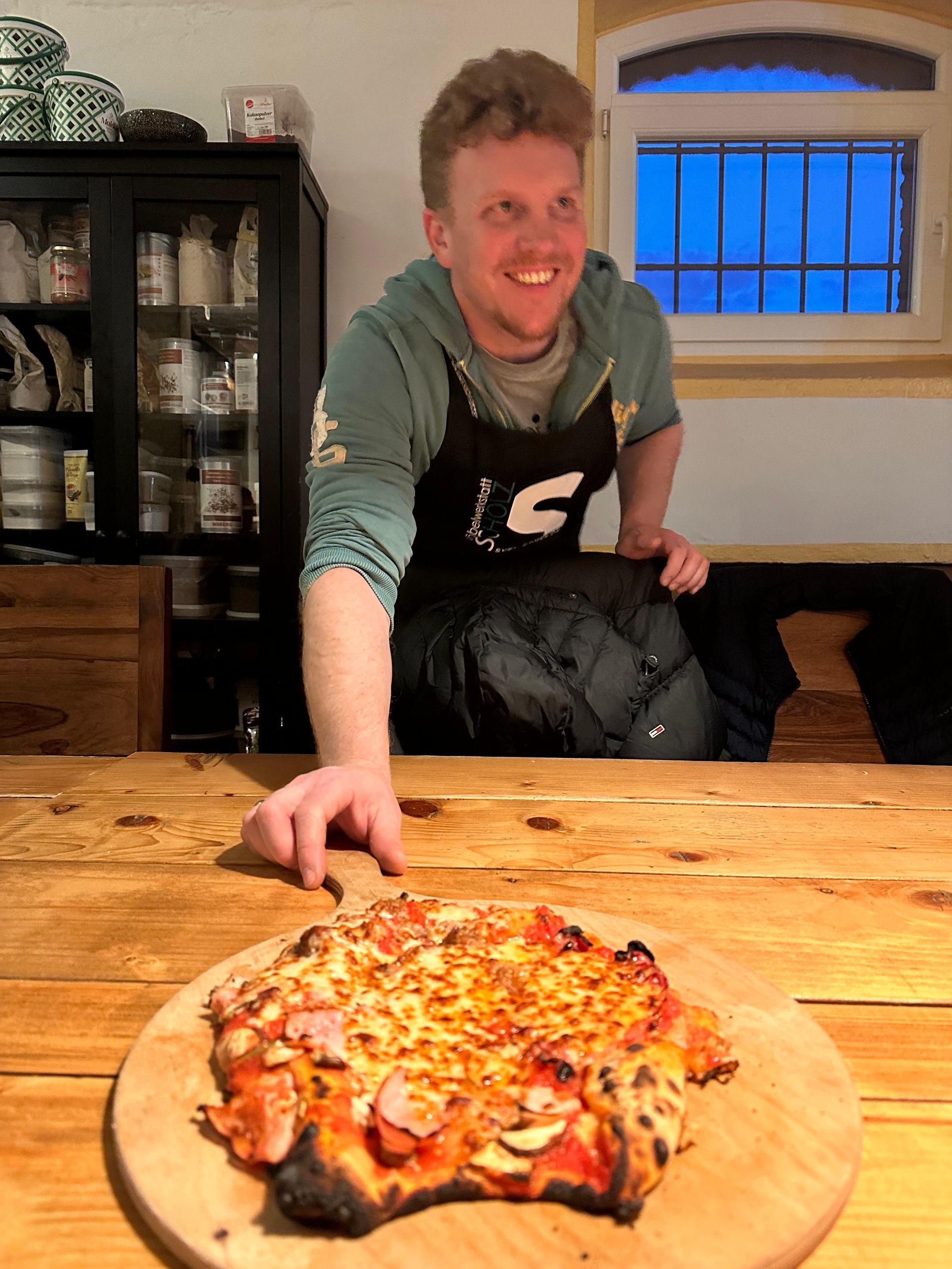 Eine Person greift in einer Küche nach einer Pizza auf einem Holzbrett.
