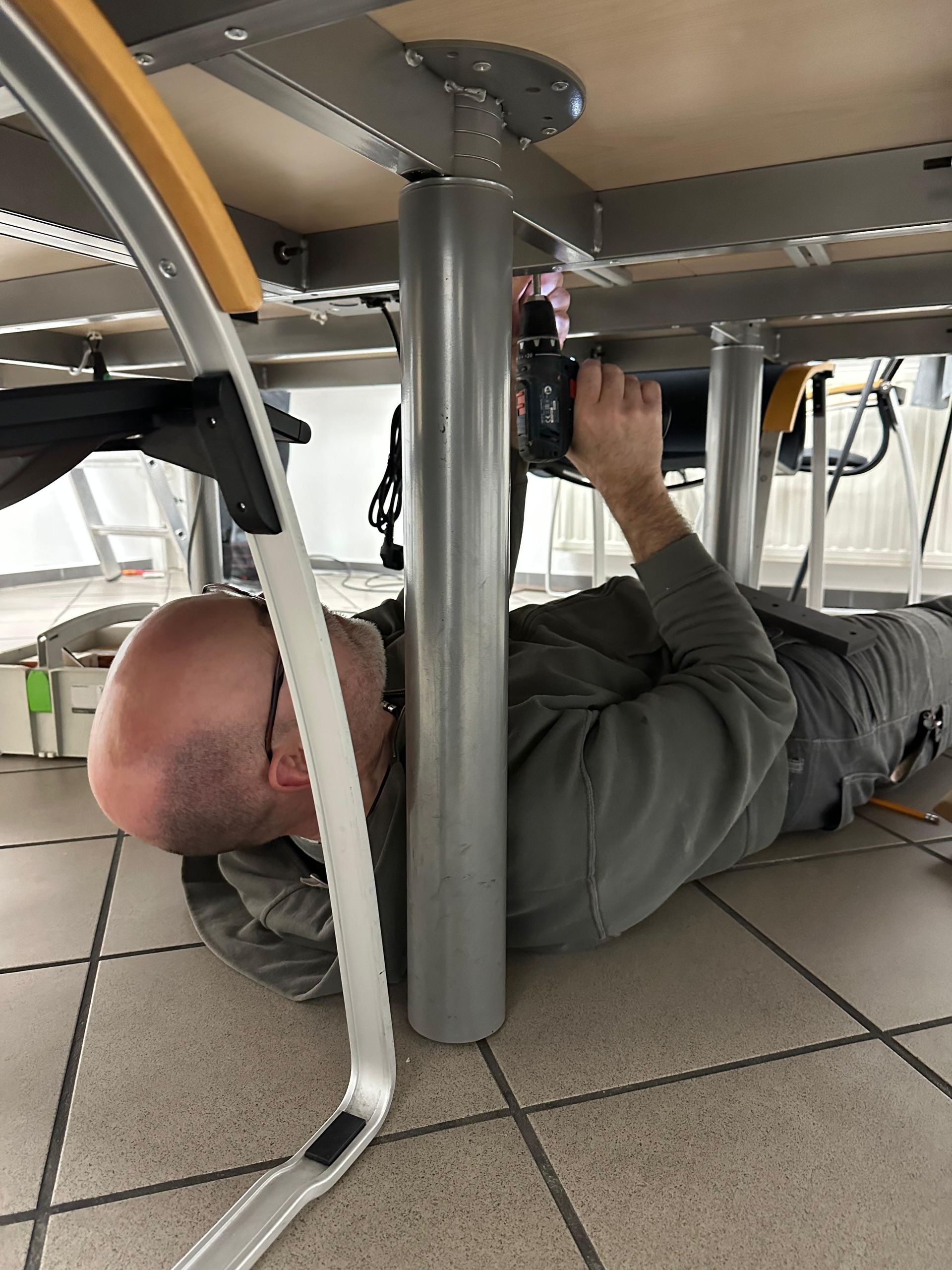 Ein Mann liegt unter einem Tisch und greift nach oben, um ein Gerät an der Unterseite zu verstellen.