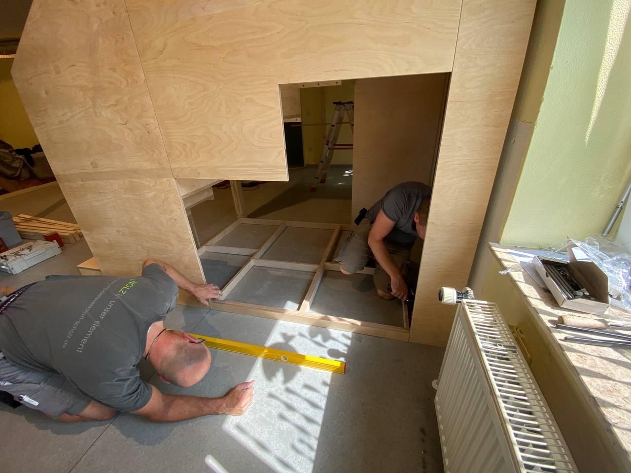 Arbeiter montieren eine Sperrholzwand und eine Türöffnung in einem im Bau befindlichen Innenraum.