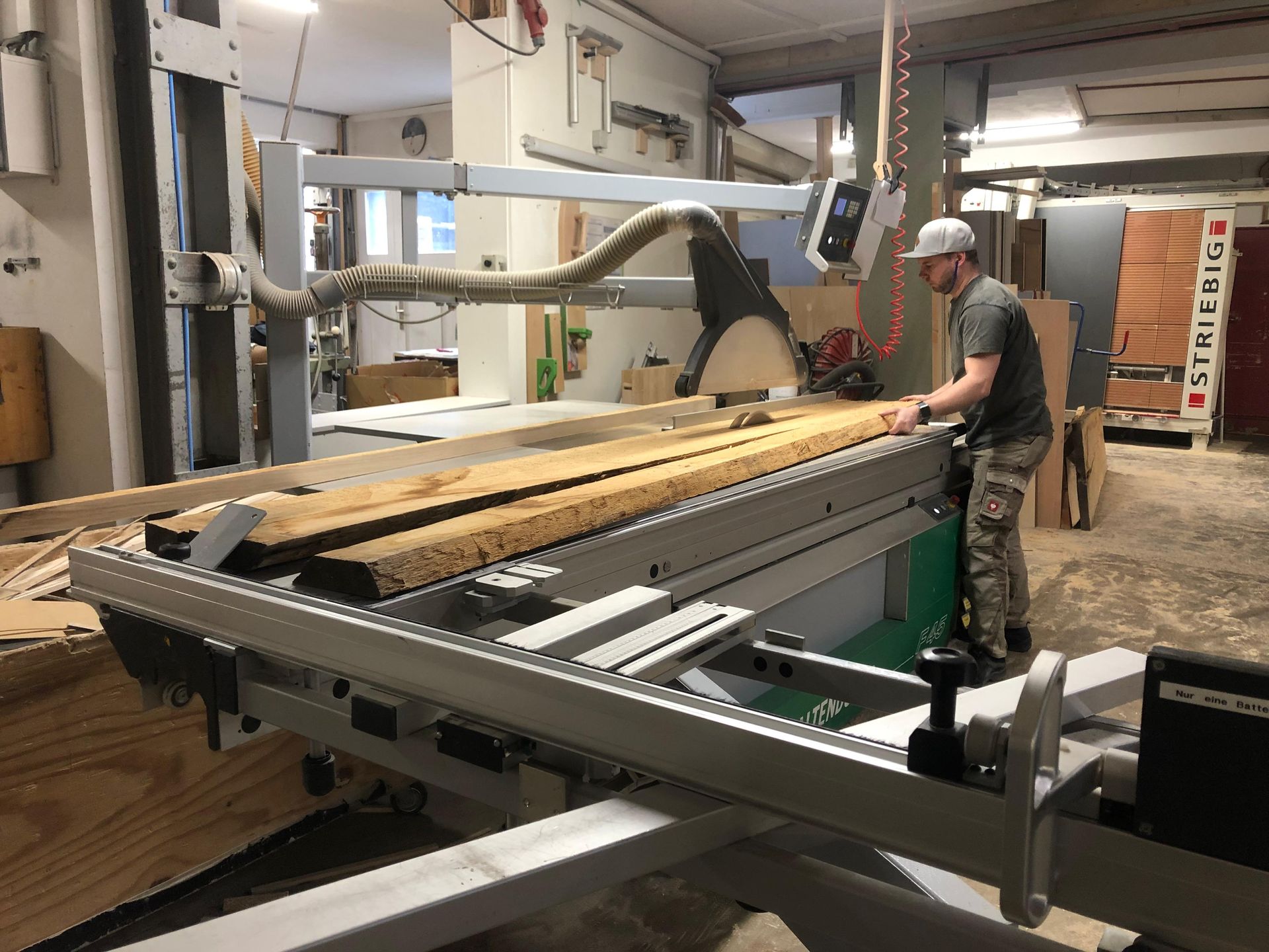 Ein Arbeiter bedient in einer Werkstatt eine große Industriesäge an langen Holzplanken.
