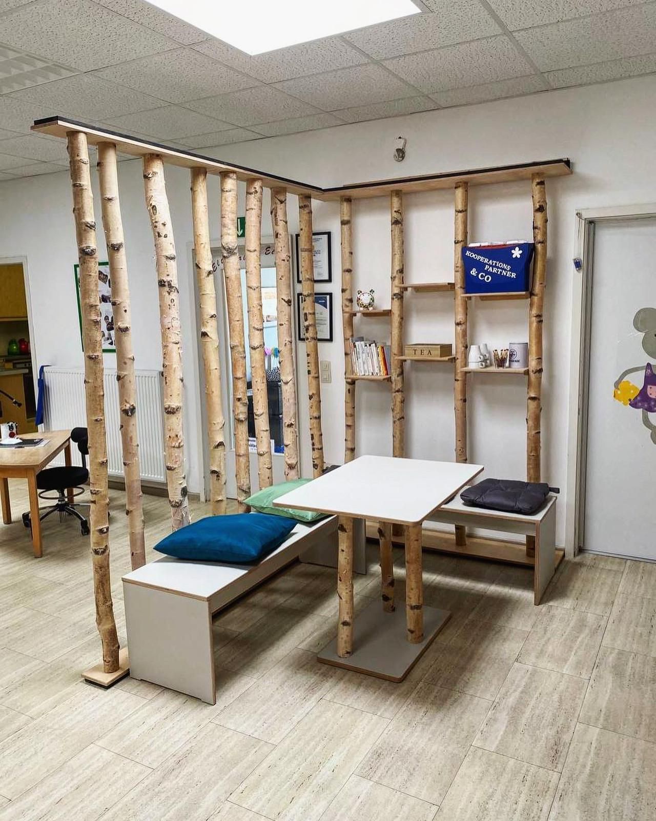 Therapieraum der Klinik mit Holzboxen, Bänken, weißem Tisch und hängenden Trainingsgeräten