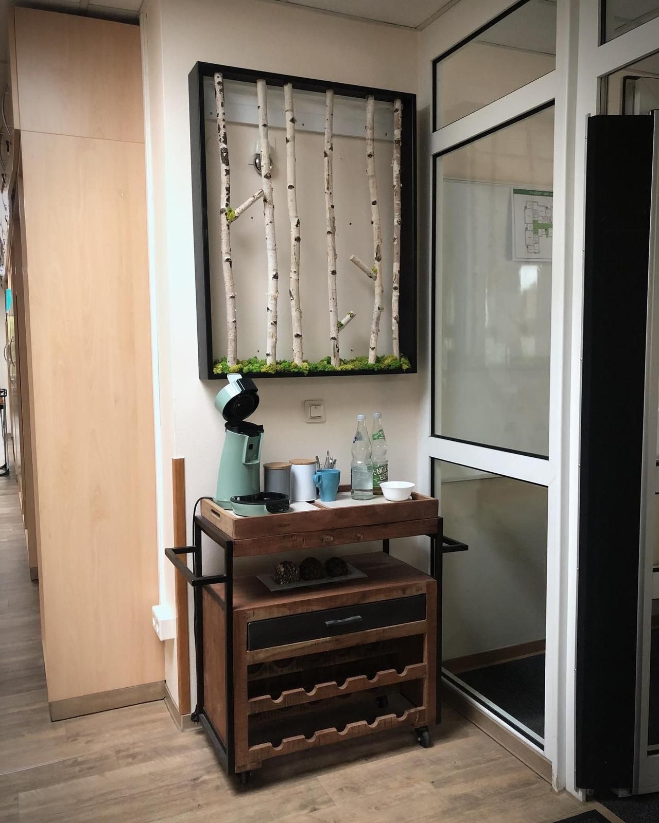 Flurecke mit hölzernem Schuhregal, kleiner Lampe, Flaschen und einer Glastür neben einem verhängten Fenster.