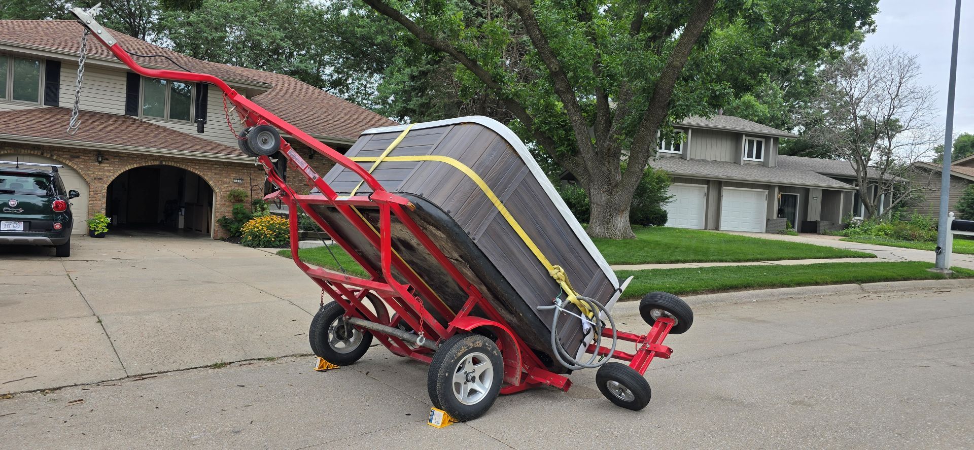 Red stair-climbing hand truck loaded with a large appliance on a suburban street