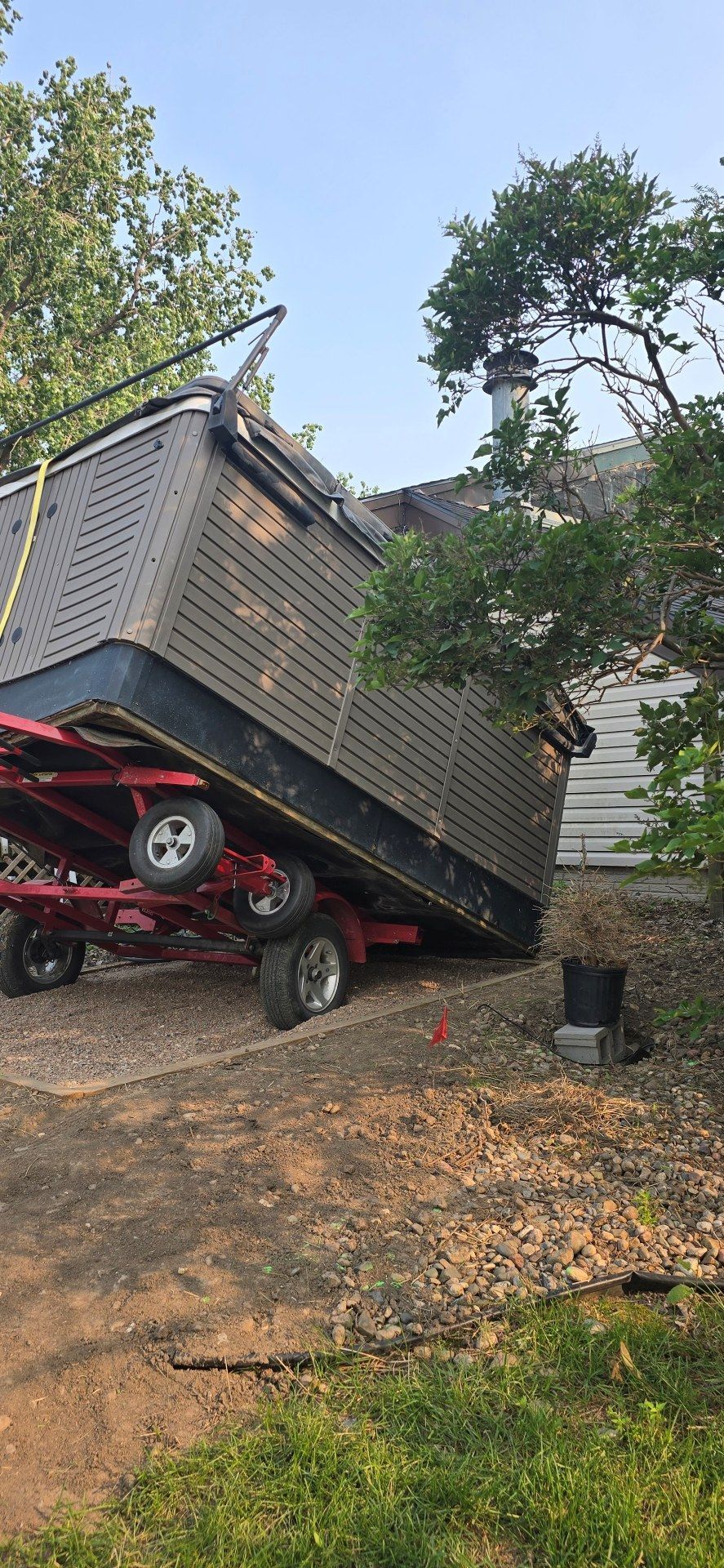 Trailer overturned in yard, leaning on a red ATV beside a house and trees.