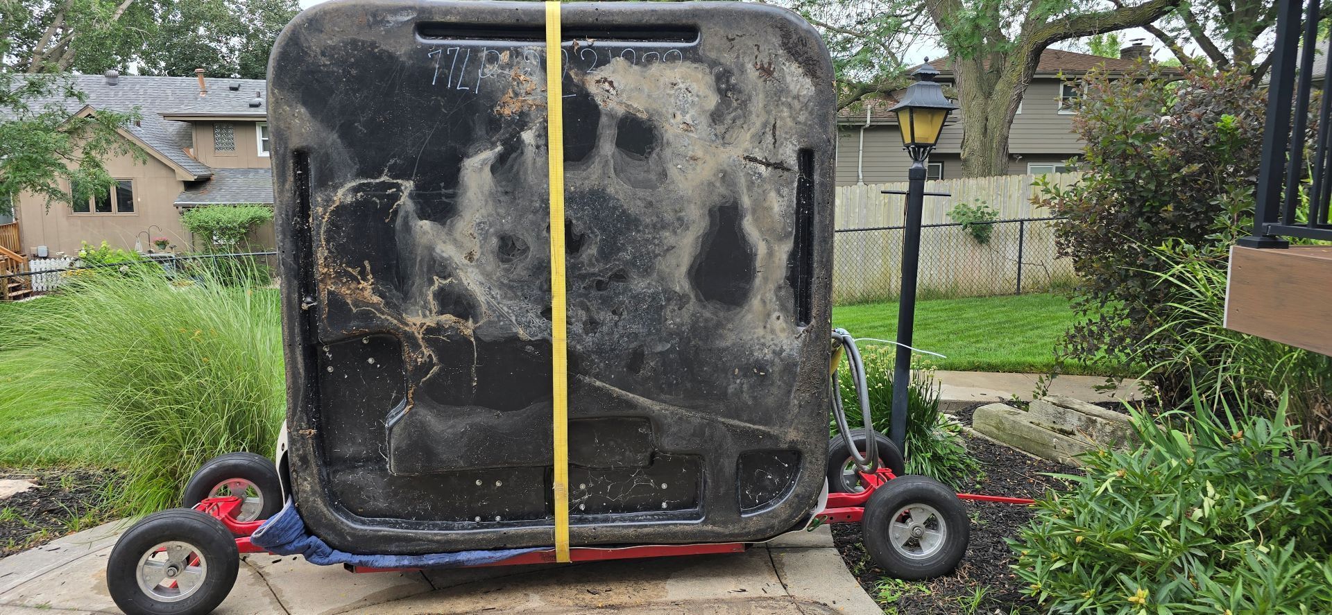 Large black hot tub strapped upright on a wheeled trailer in a backyard