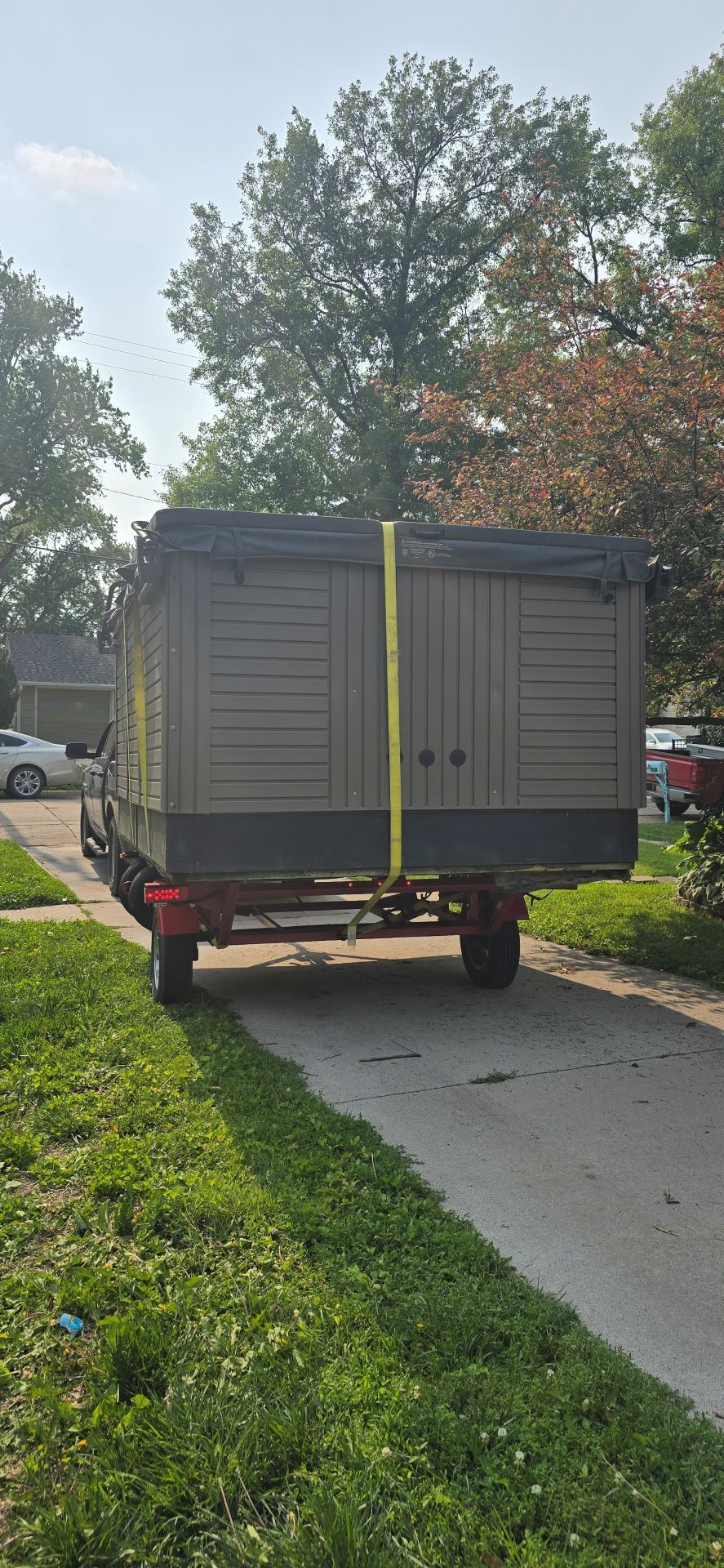 Gray storage trailer parked on a sidewalk beside a grassy yard and trees