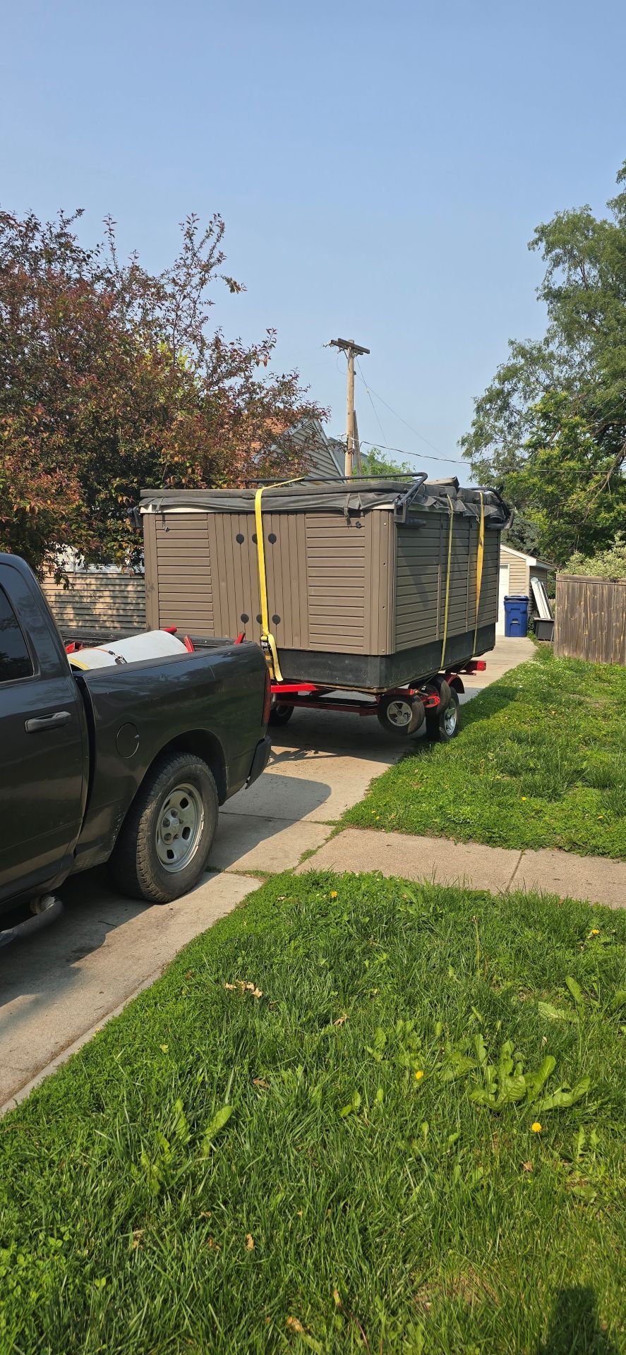 Pickup truck towing a trailer with stacked boxes on a suburban street beside a sidewalk and grass.