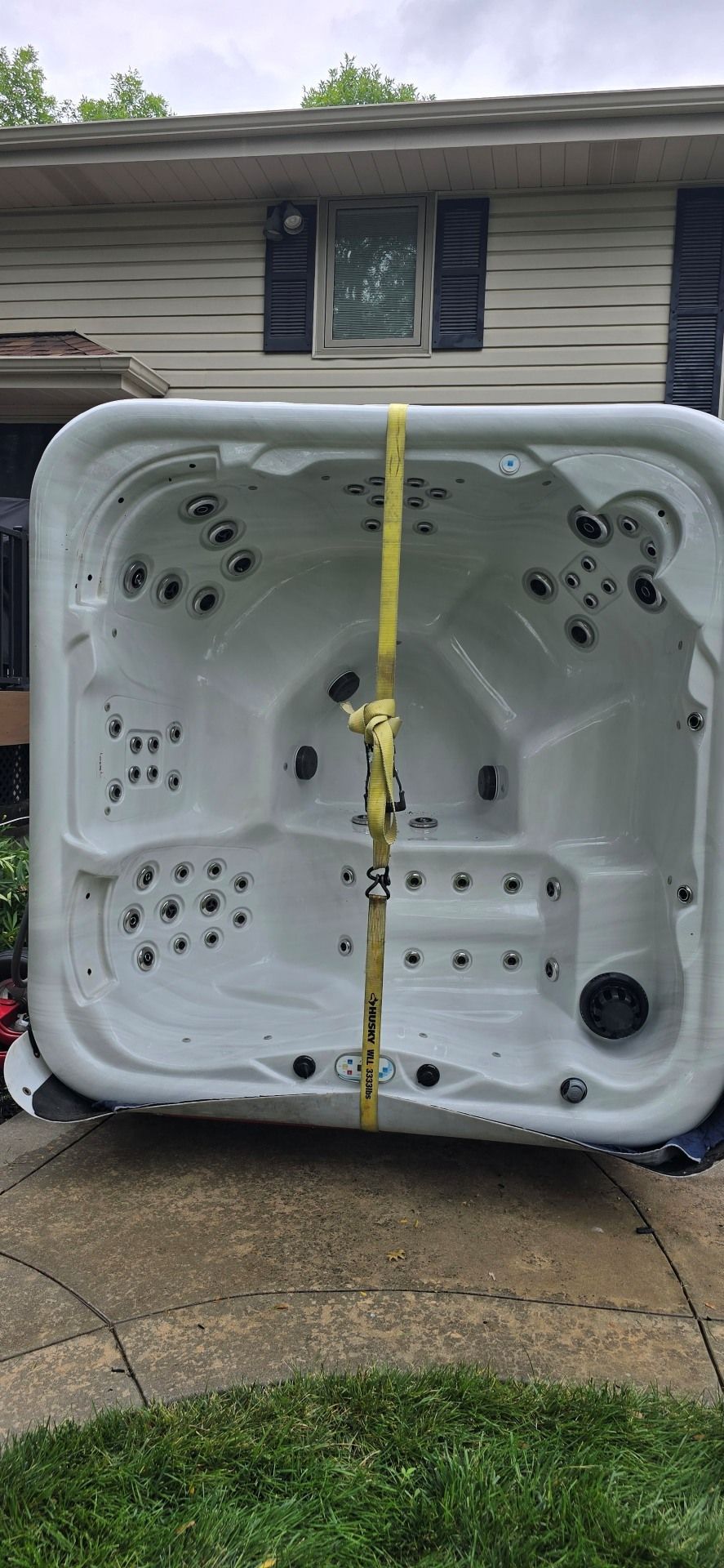 White hot tub flipped on its side in a driveway, with a yellow strap in front of a house.