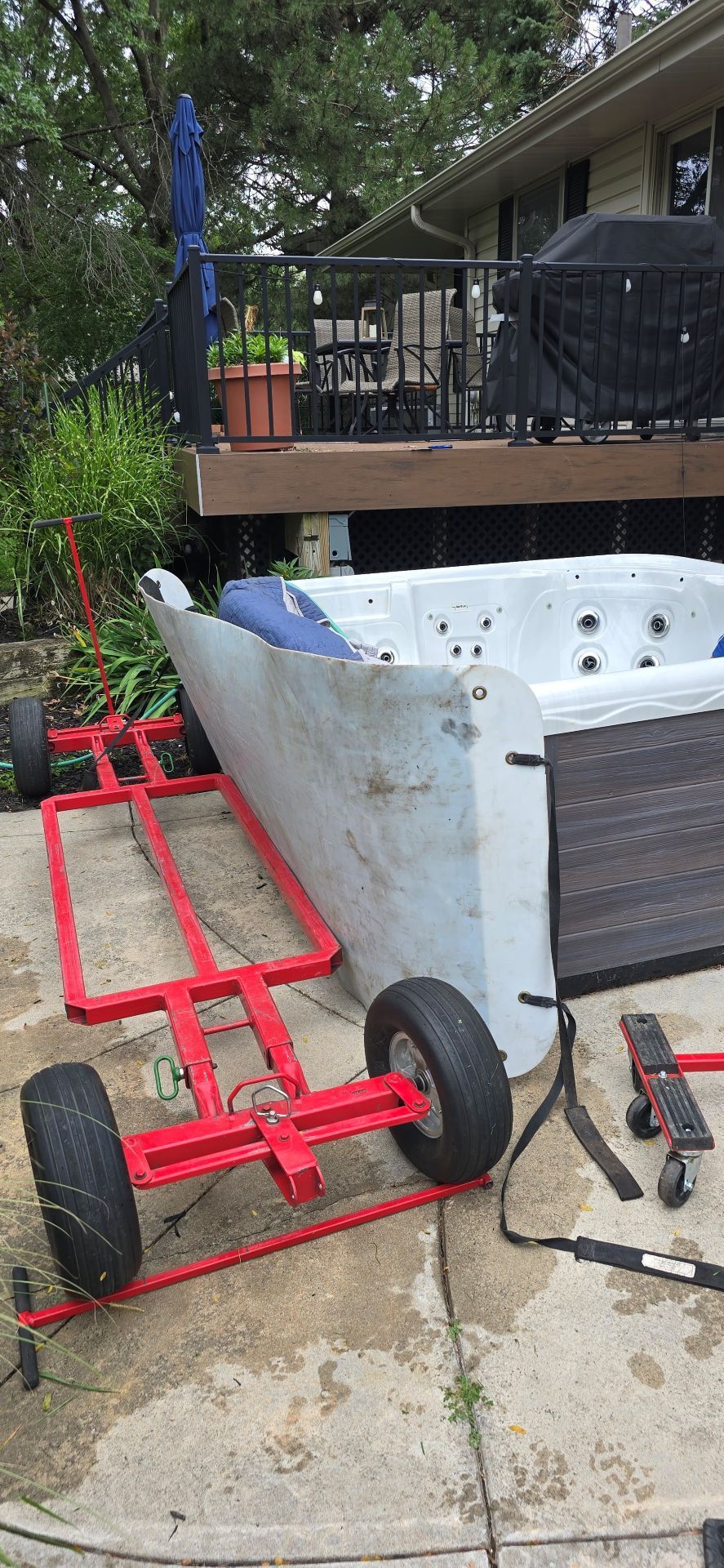 Red garden cart with black wheels and a white tub on a concrete driveway beside a porch.