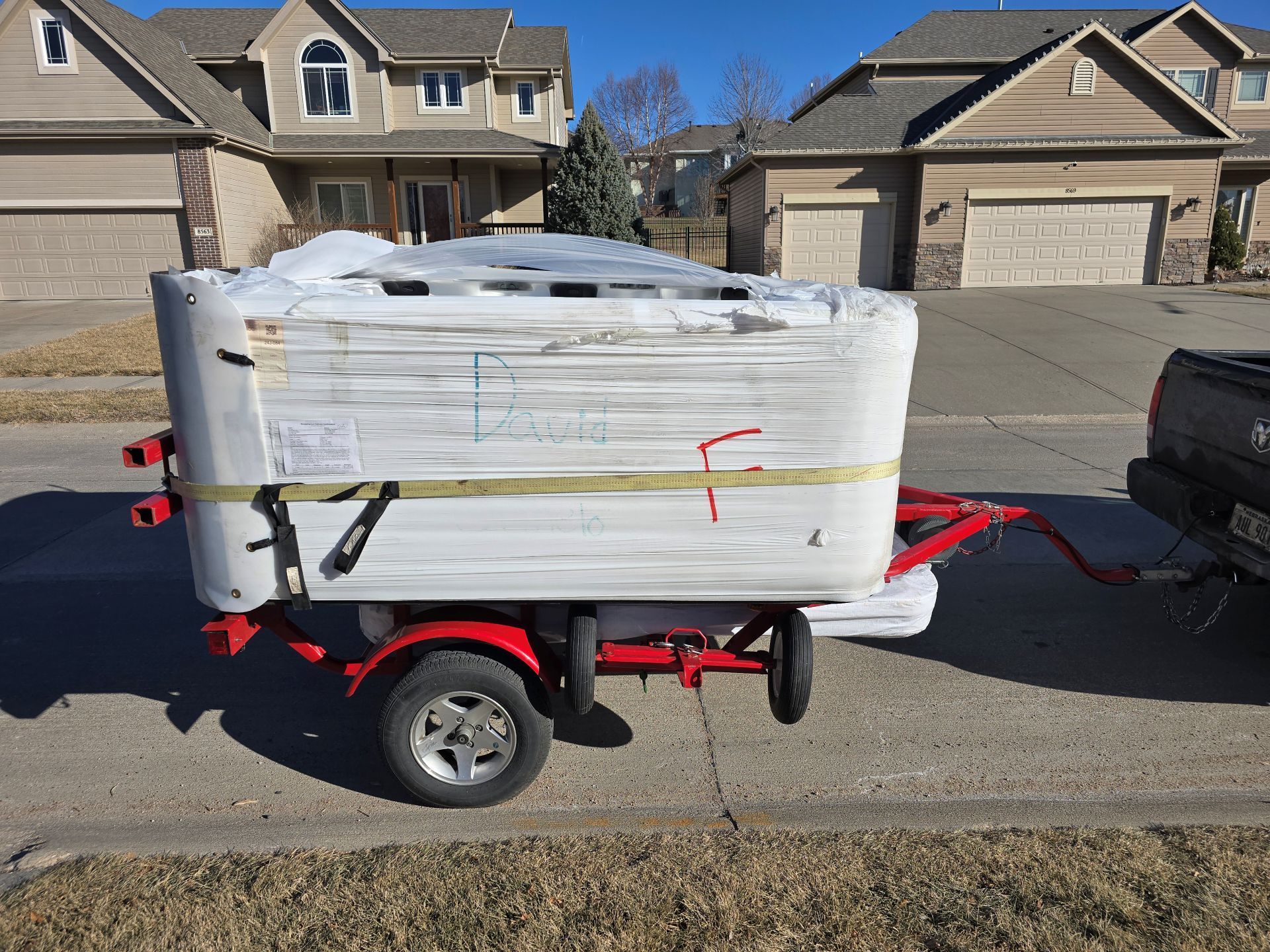 Wrapped white cargo on a red utility trailer parked on a suburban street, with a pickup truck attached.