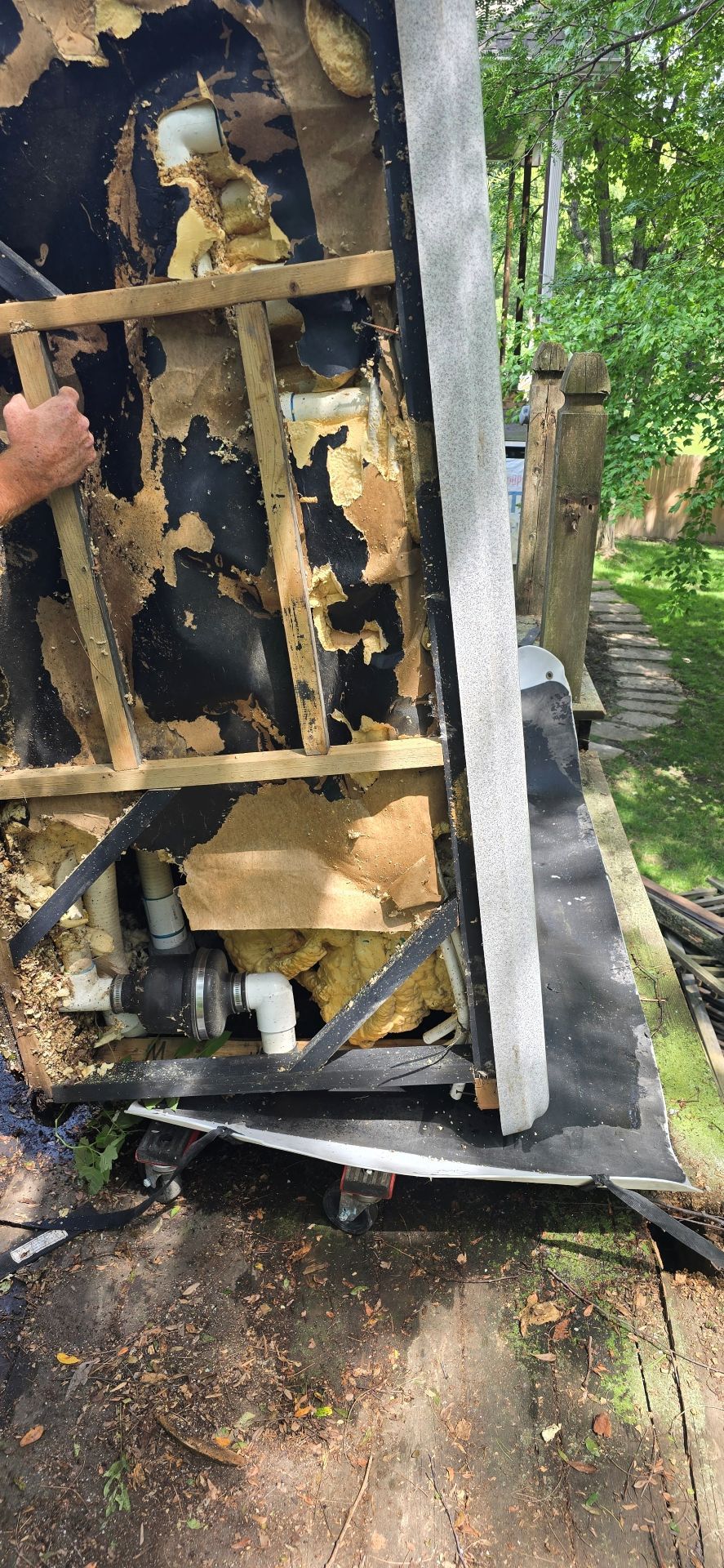 Charred refrigerator lying on its side outdoors, with burned debris and trees in the background.