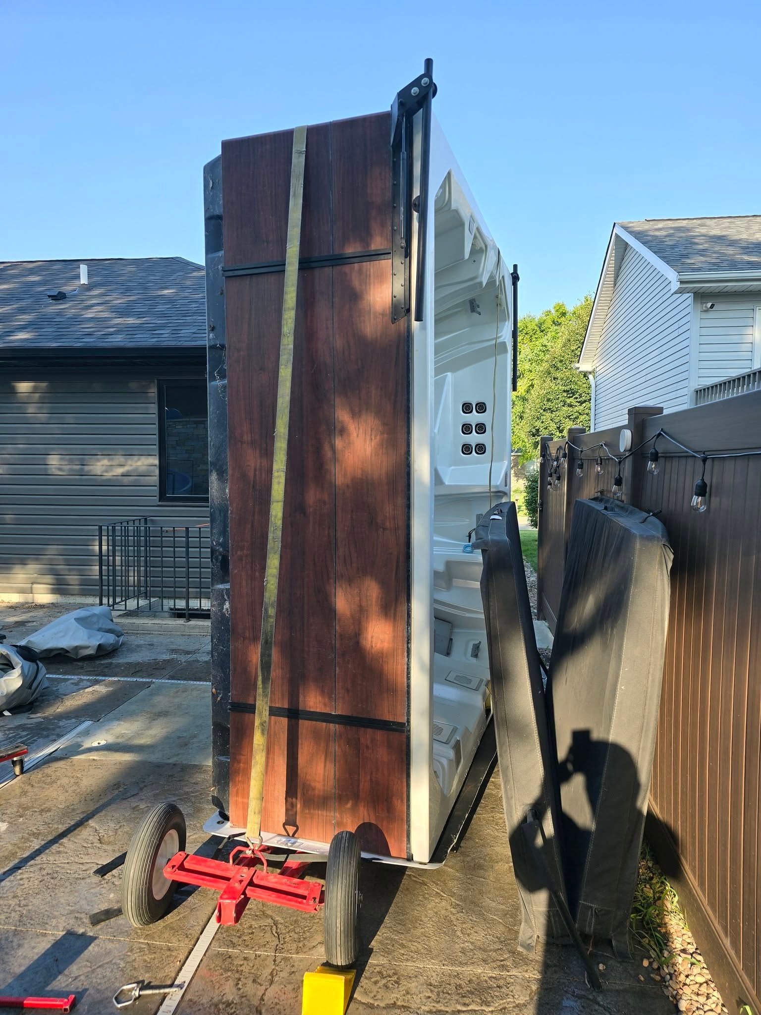 Tall rusted metal cabinet beside a house, strapped to a dolly in a narrow outdoor alley.