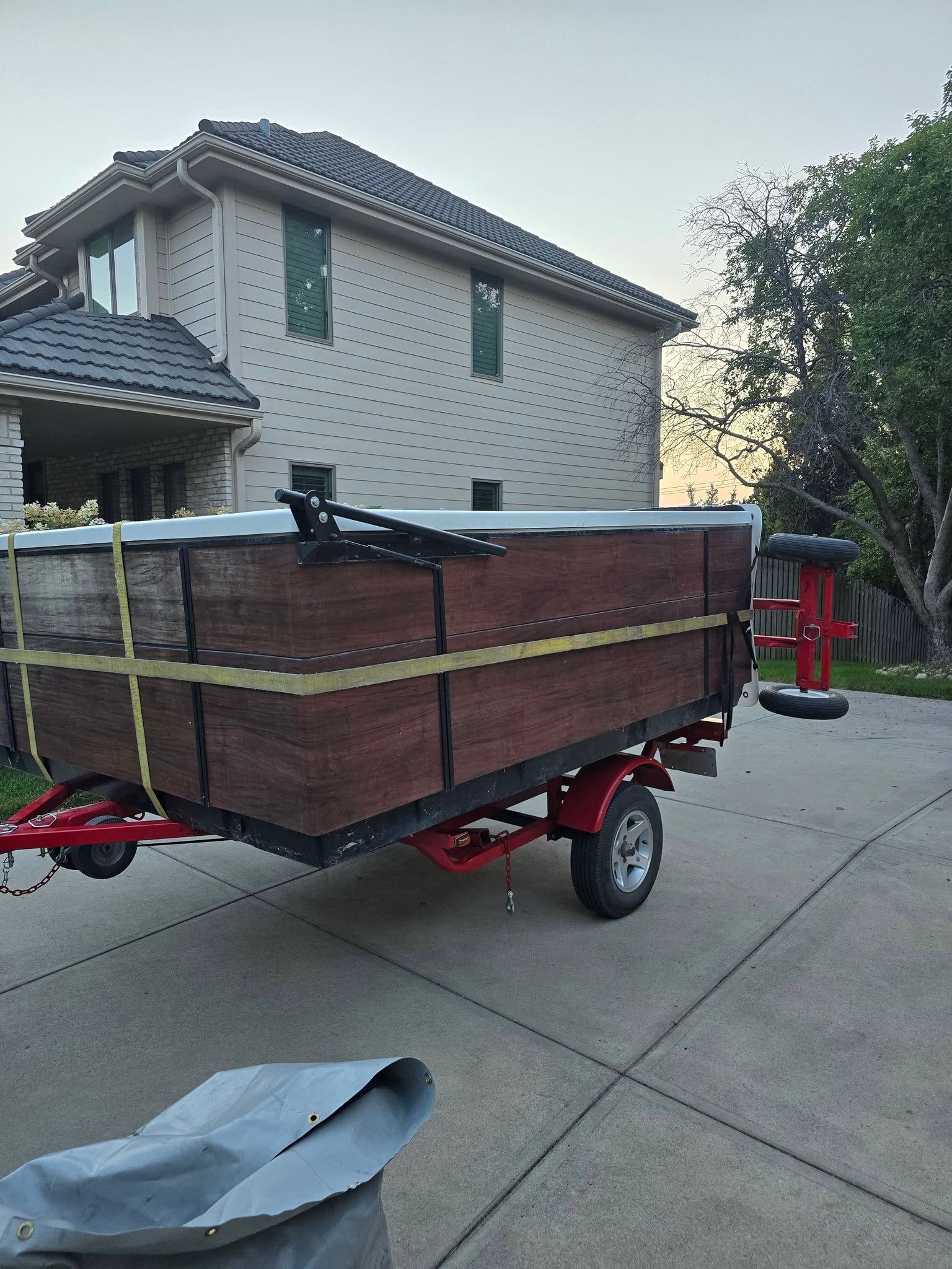Red utility trailer with wooden sides parked on a driveway beside a house