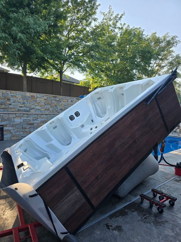 Tipped-over outdoor hot tub with white interior and dark wood siding in a backyard.