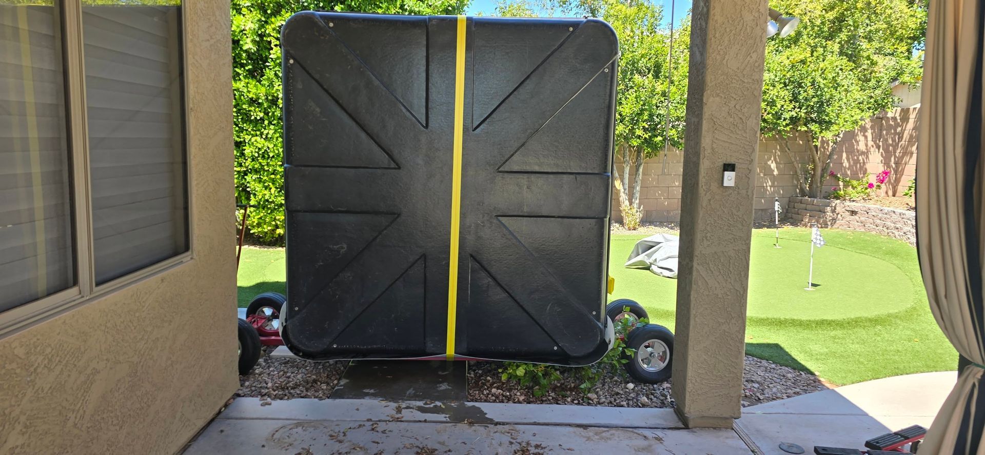 Closed black gate with a yellow center stripe beneath a covered patio, opening to a green yard