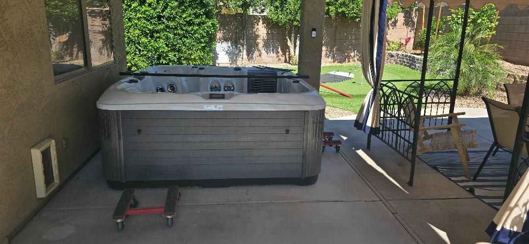 Hot tub on a covered patio beside a house, with a scooter in front and lounge chairs in the background