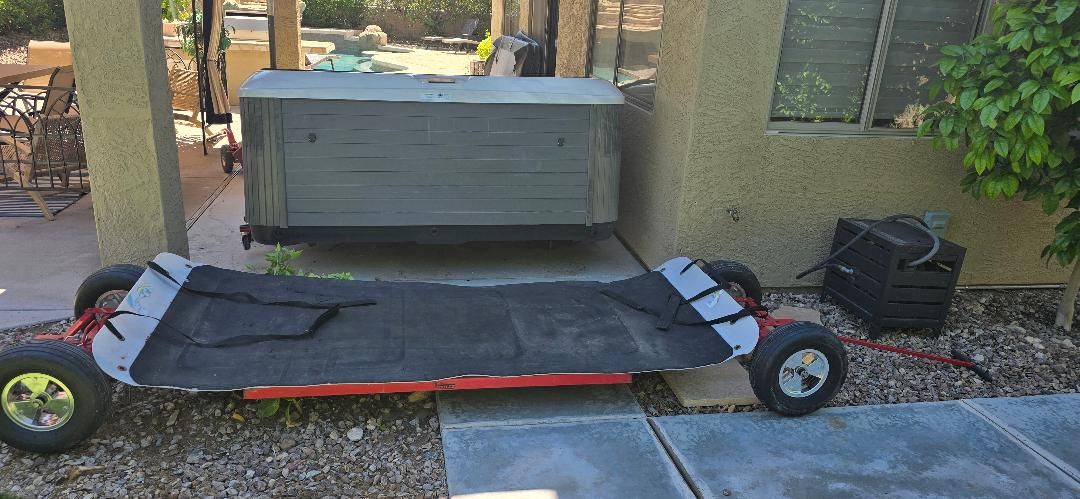 Black utility cart with large wheels parked outdoors beside a wall and planter boxes.