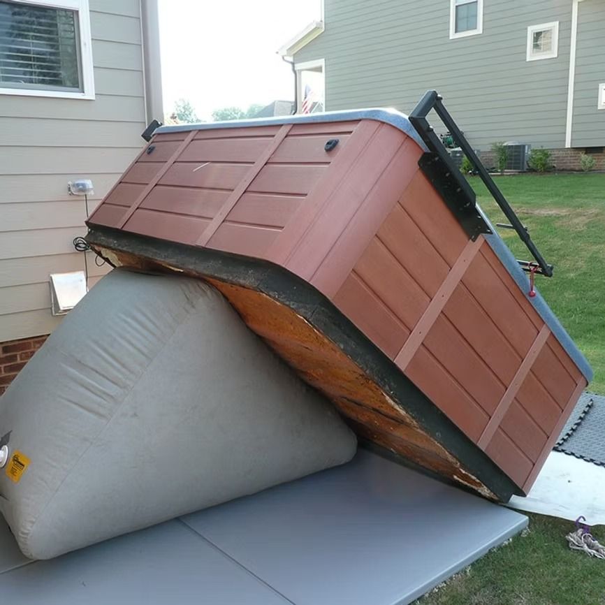 A tipped-over brown shed-like structure resting on a large gray cushion in a backyard.