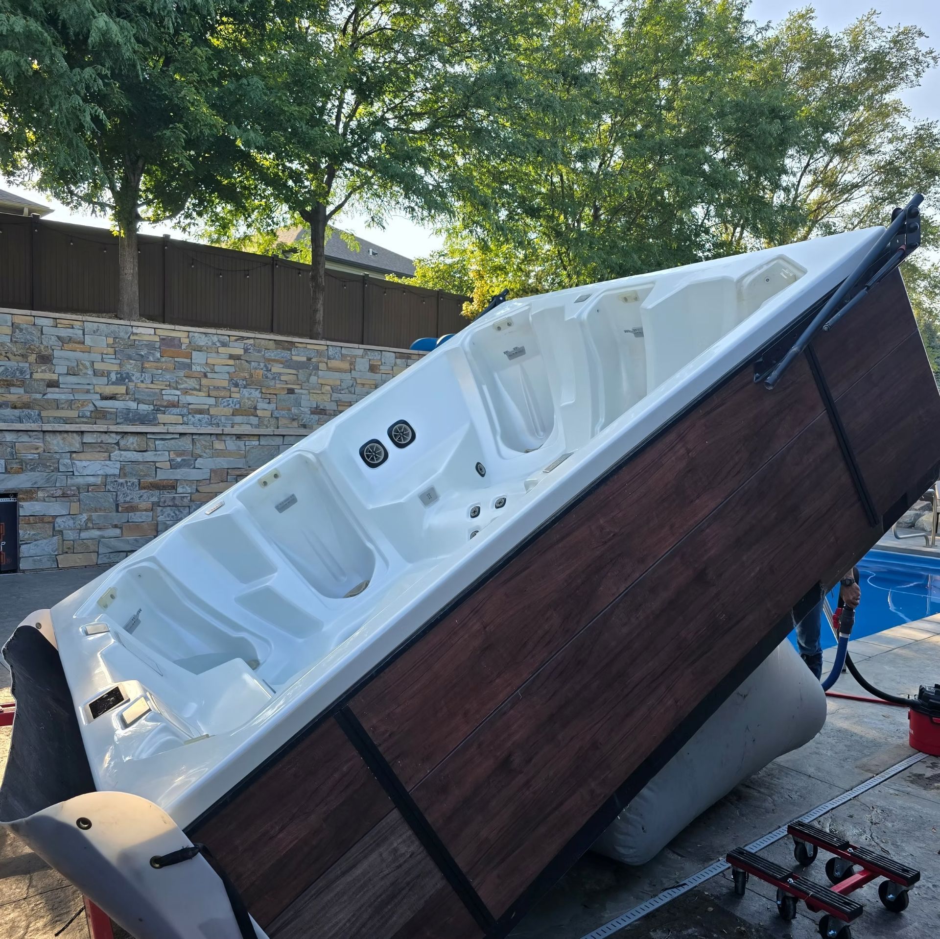 Tipped-over white hot tub with wood paneling in a backyard, propped on its side during repair or removal