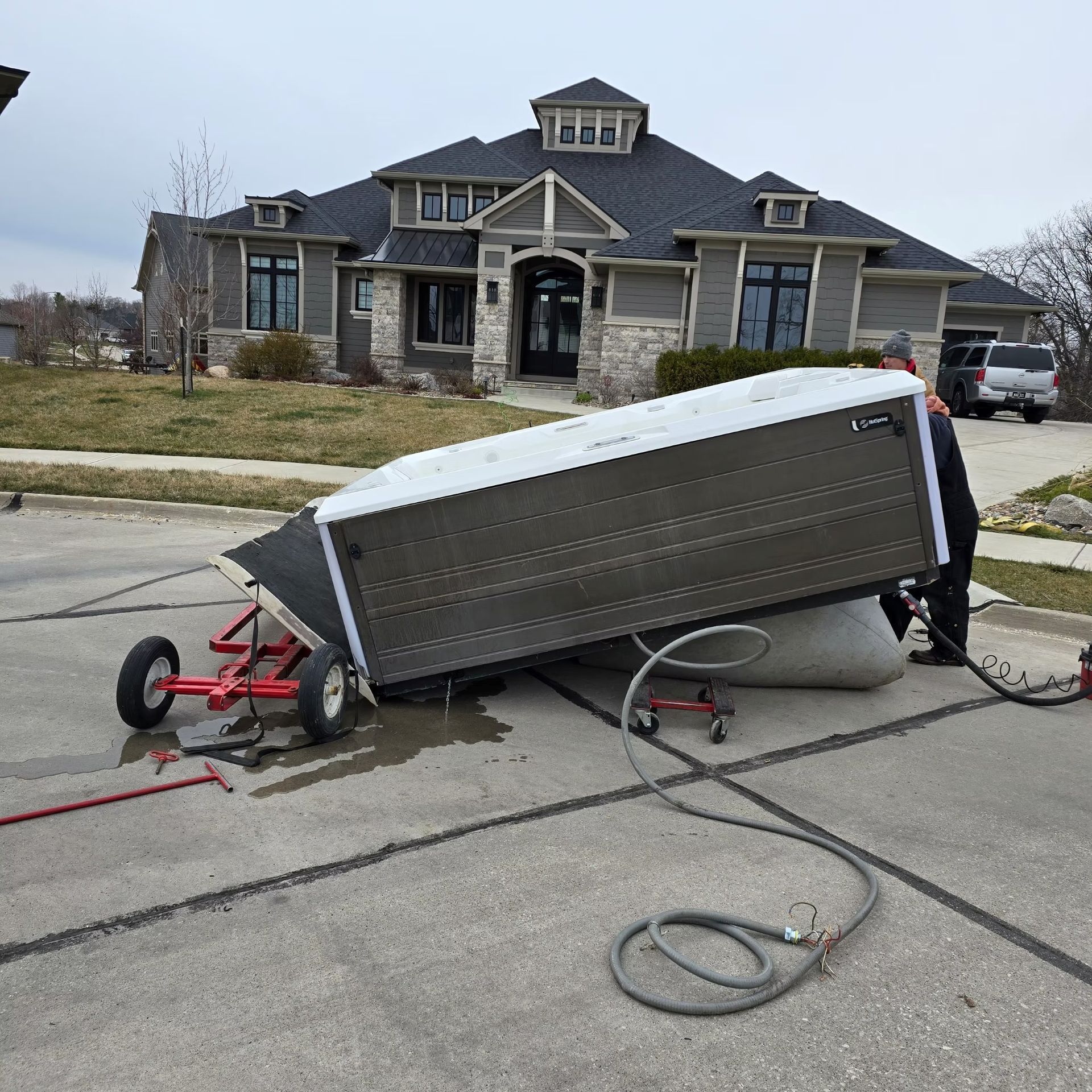 Collapsed trailer on a suburban street in front of a house, with a detached wheel and hitch.