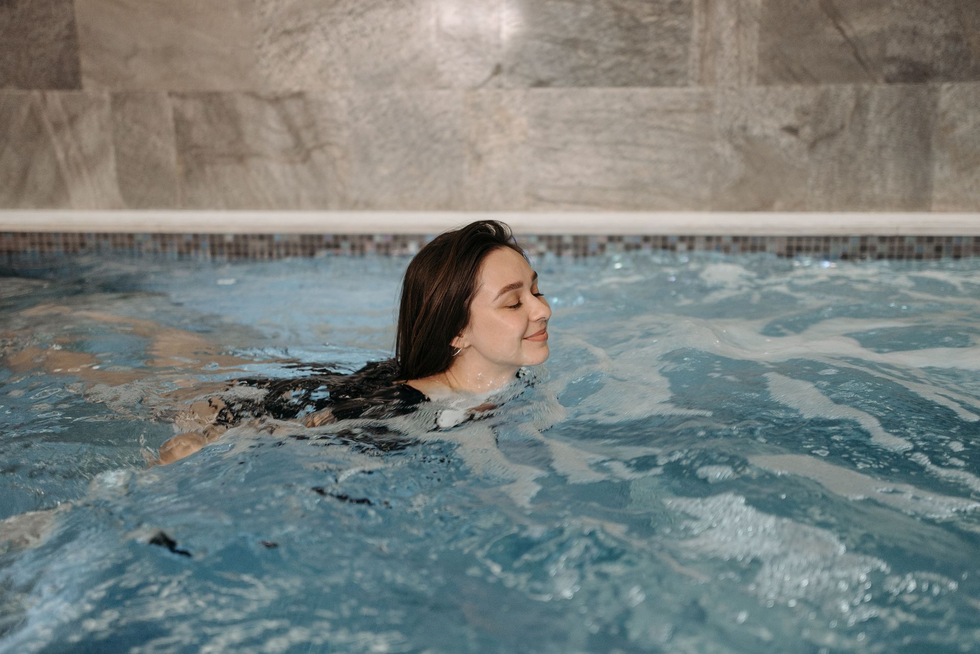 Person swimming in an indoor pool, smiling near the surface.