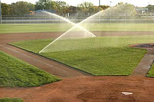 Two sprinklers are spraying water on a baseball field.