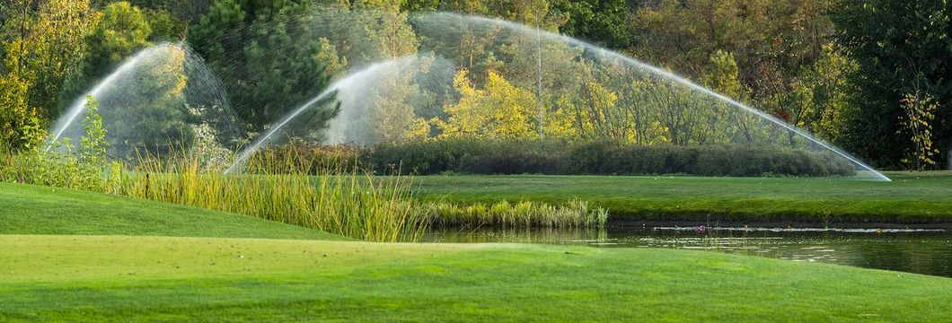 A couple of sprinklers spraying water on a lush green field.