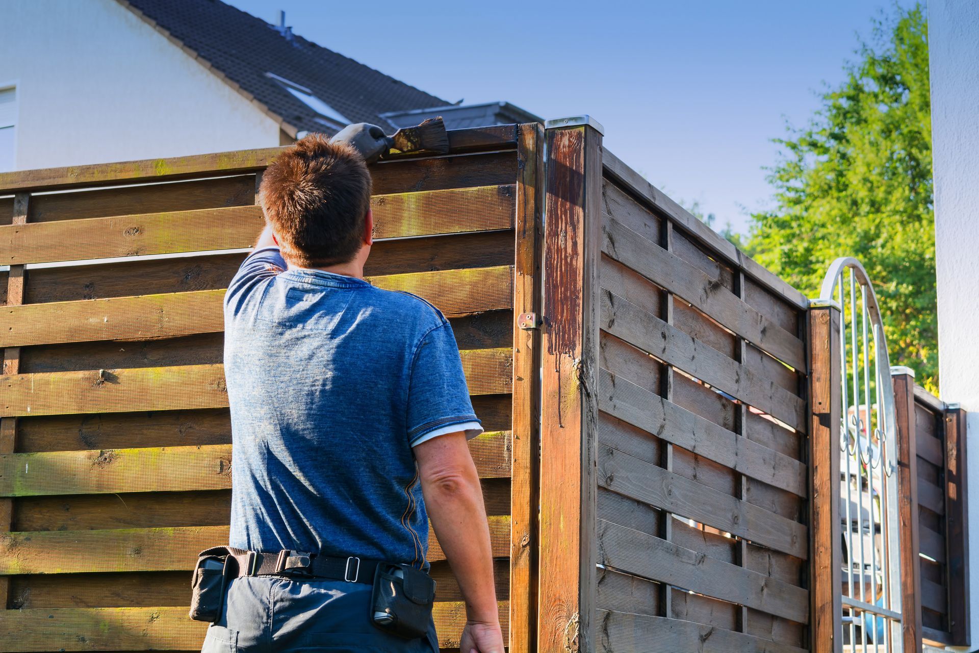 A man in a blue shirt is standing next to a wooden fence.