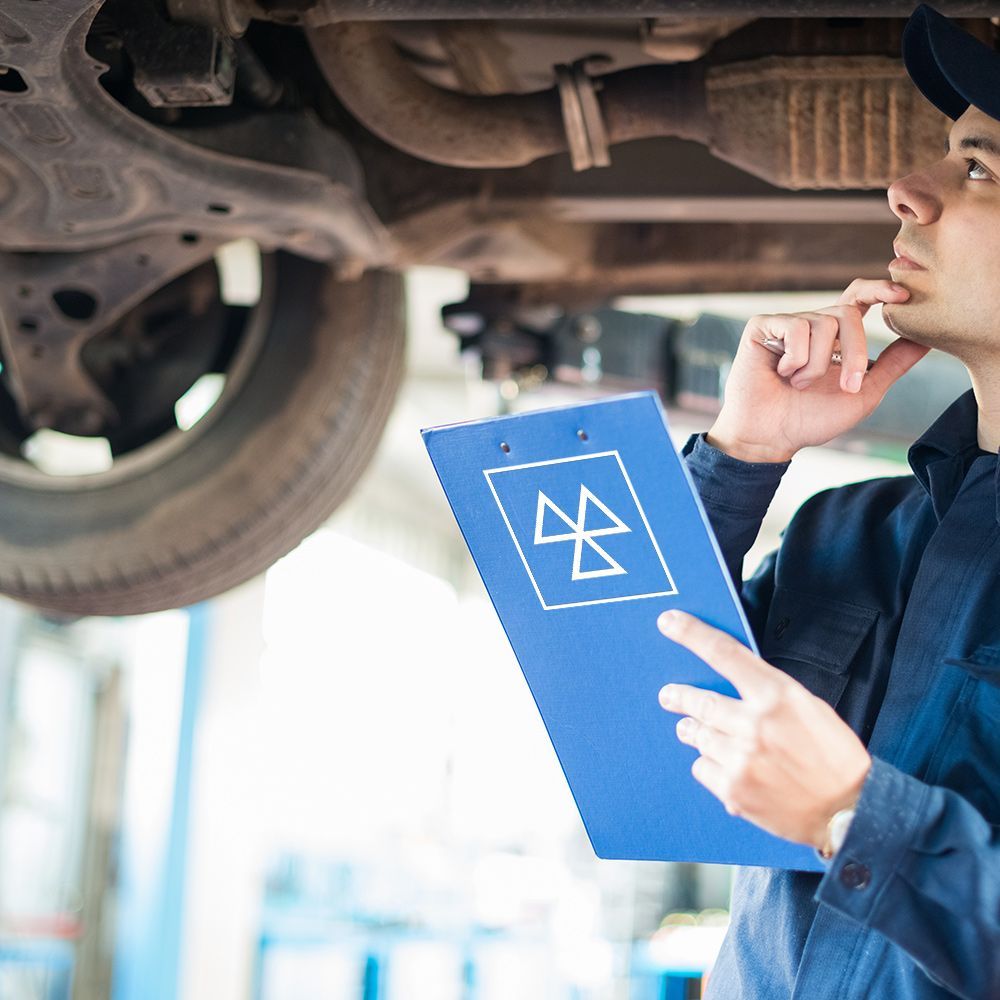 a man is looking under a car while holding a clipboard