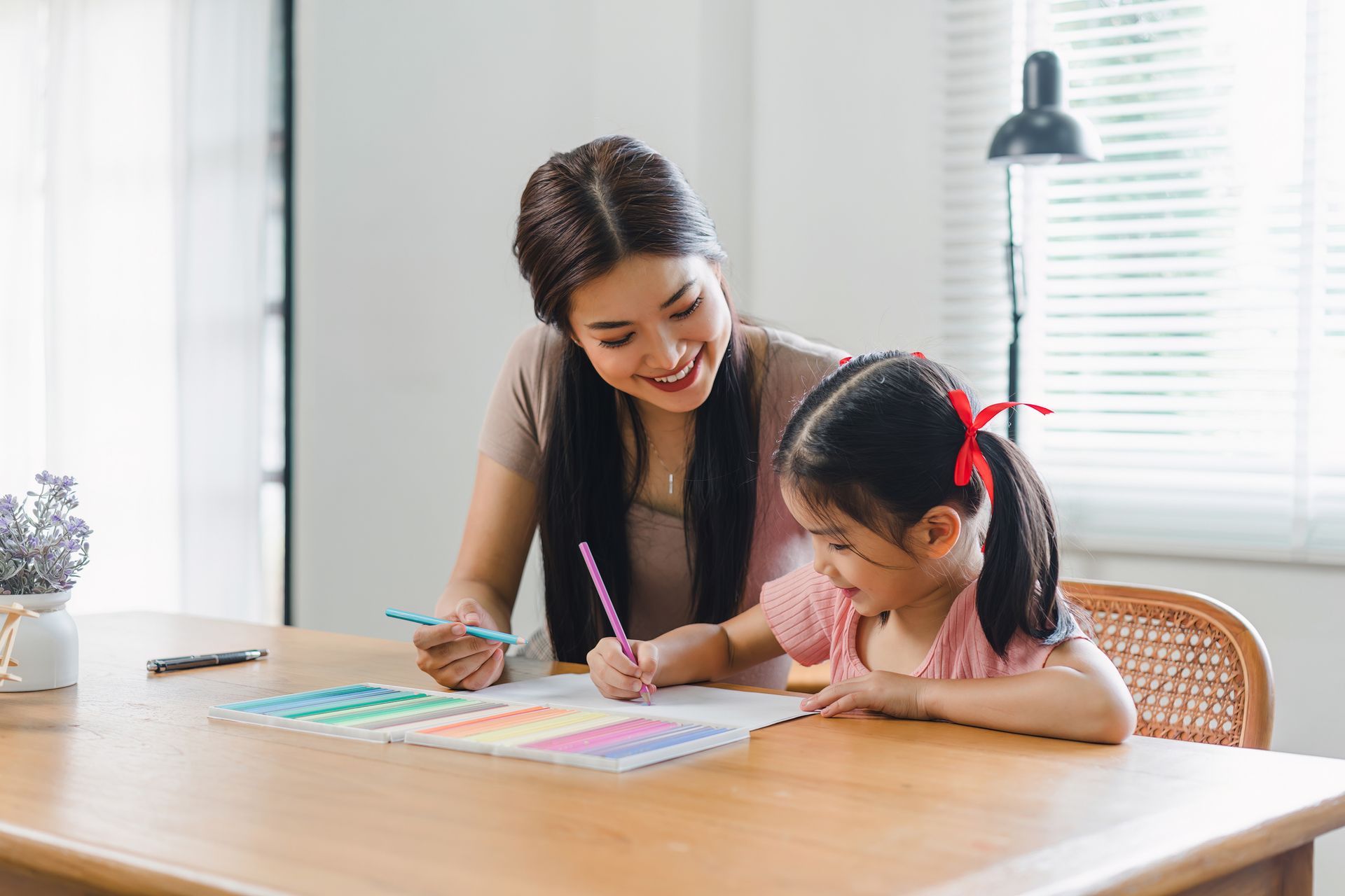 Woman and child drawing together at a table in a bright room