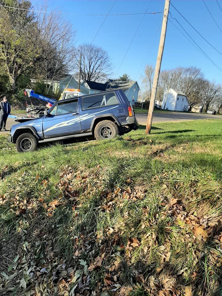 A blue jeep is parked on the side of the road in a grassy field.