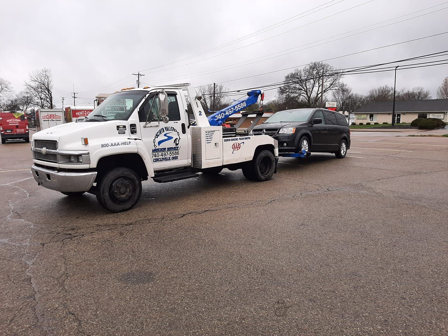 A white tow truck is towing a black car in a parking lot.