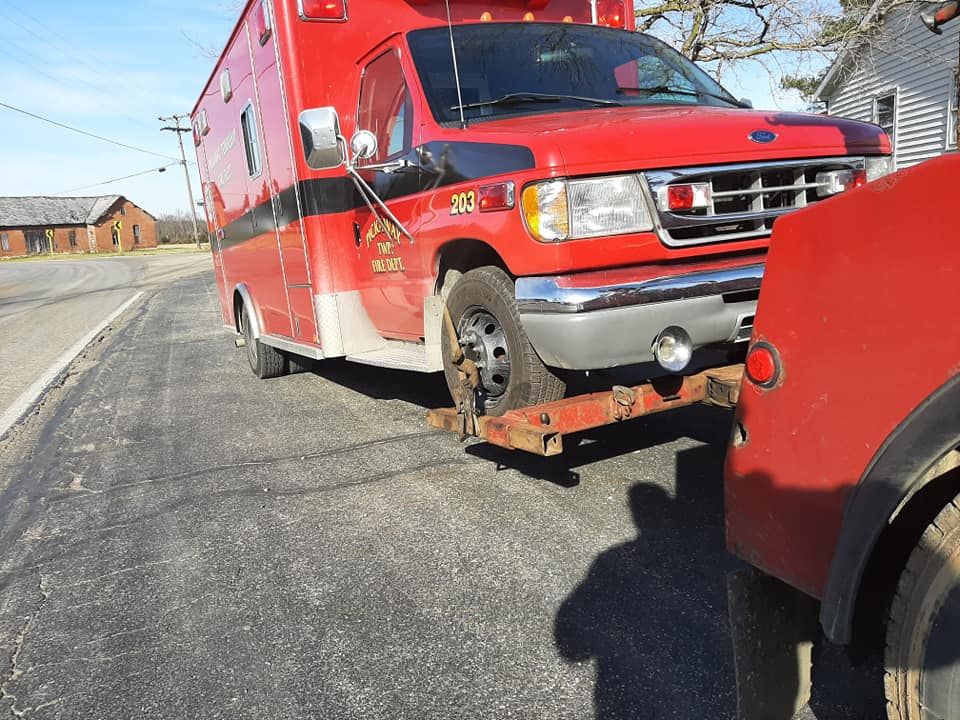 A red ambulance is being towed by a tow truck