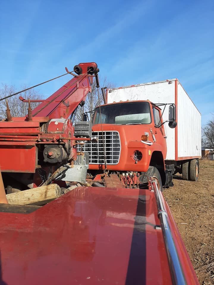 A red tow truck is towing a white truck in a field.